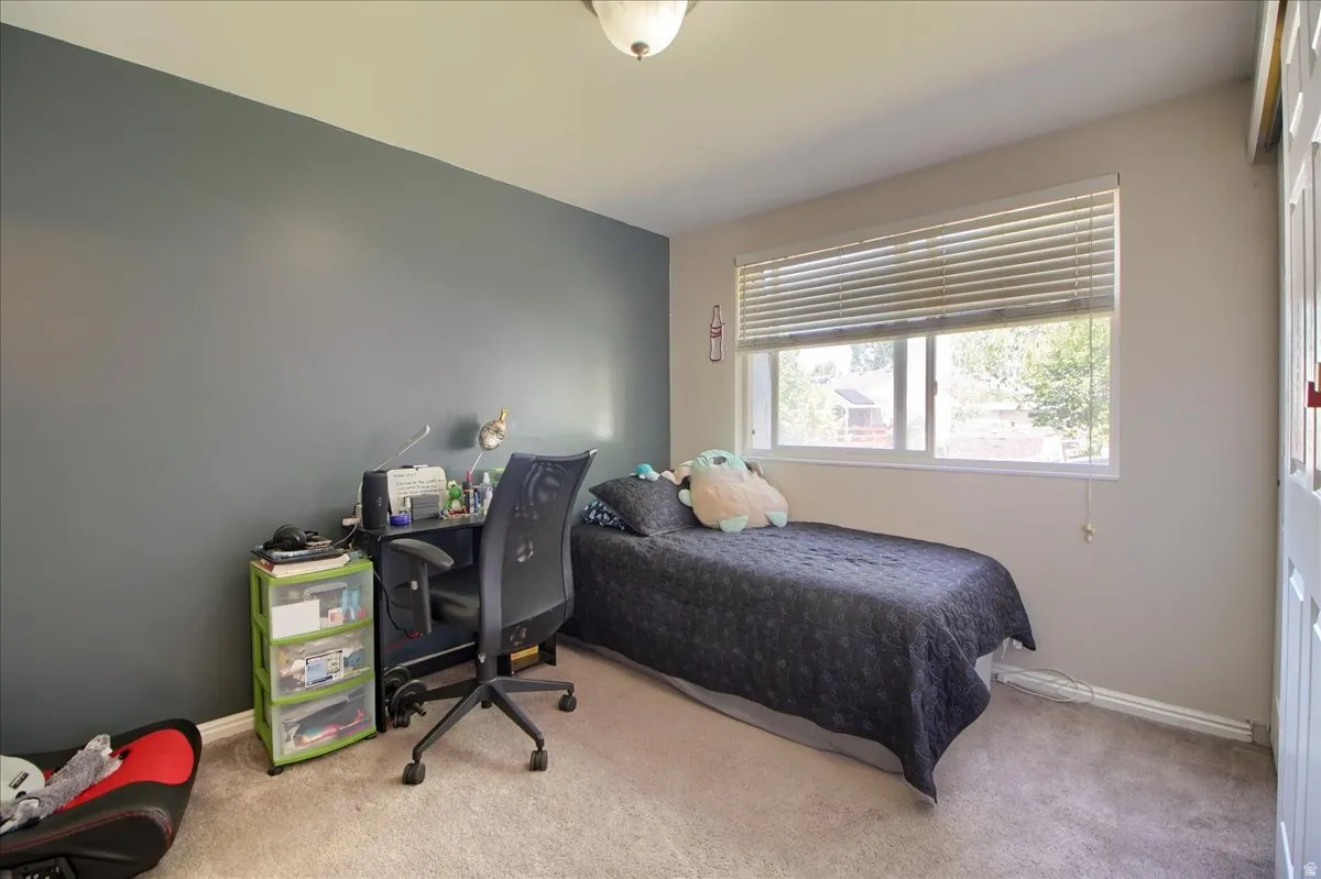 Bedroom featuring a large window with horizontal blinds, carpeted flooring, and a wall-mounted light fixture