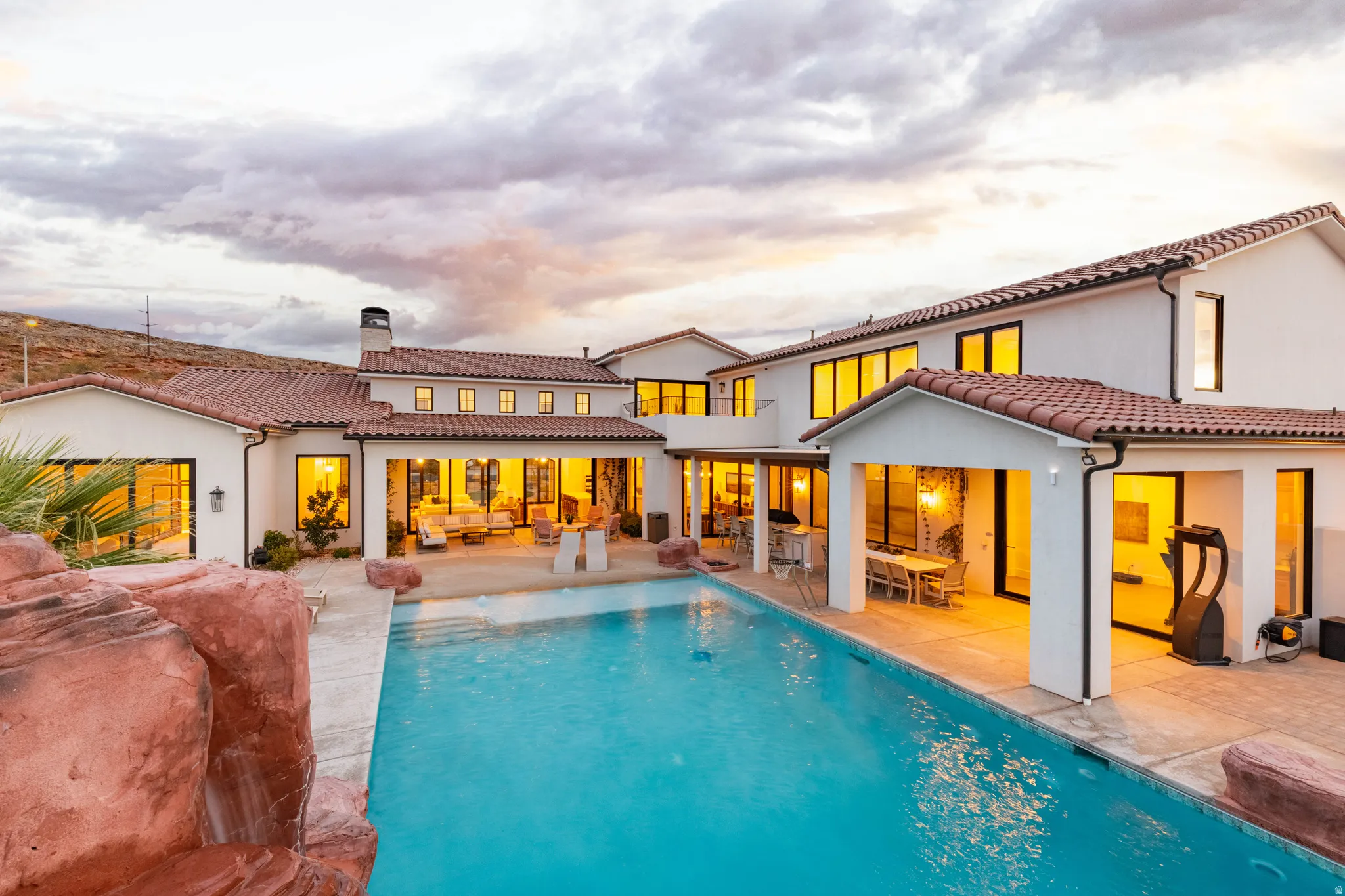 Back of house at dusk featuring a patio area, outdoor lounge area, an outdoor pool, a tiled roof, and a chimney