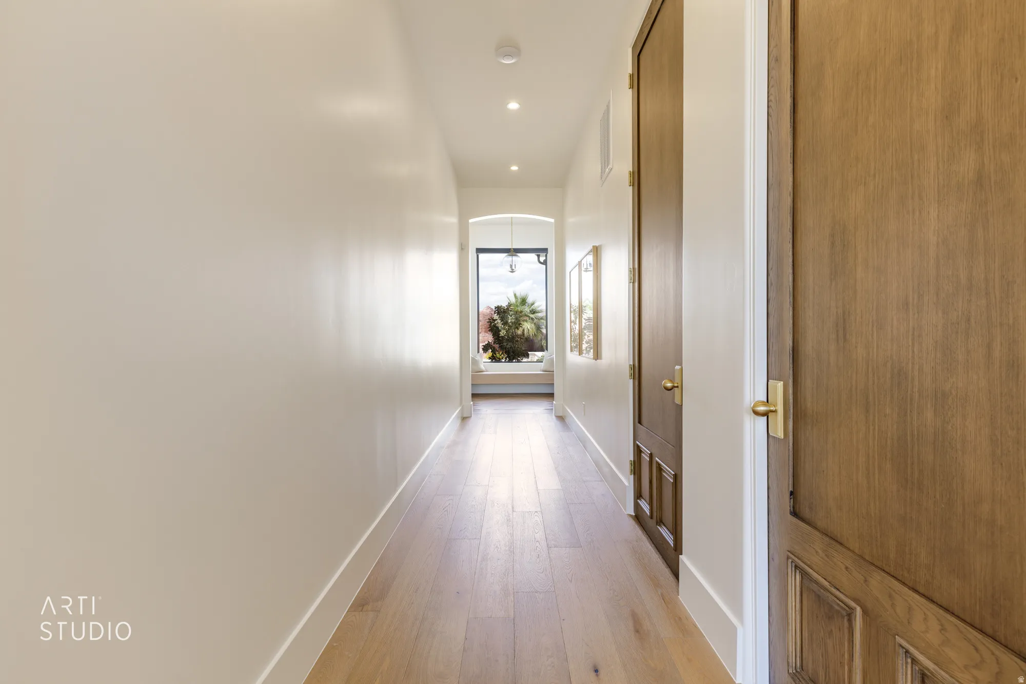 Hallway featuring light wood-finish flooring, recessed lighting, and solid core doors with brass hardware
