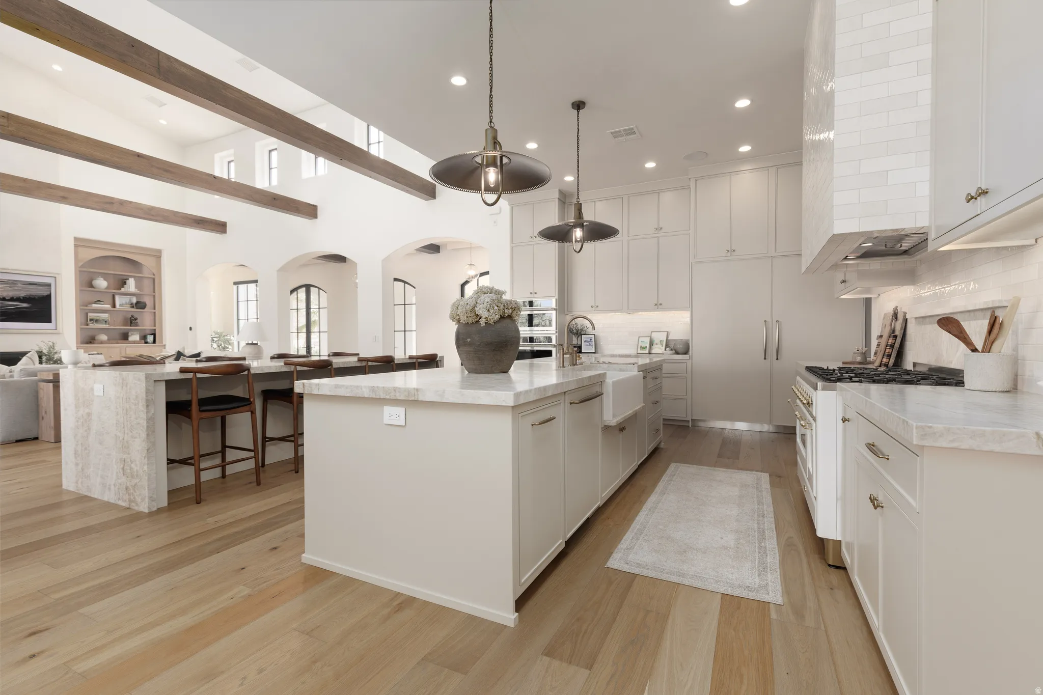 Kitchen featuring open floor plan, range with gas stovetop, arched walkways, light wood finished floors, and light stone countertops
