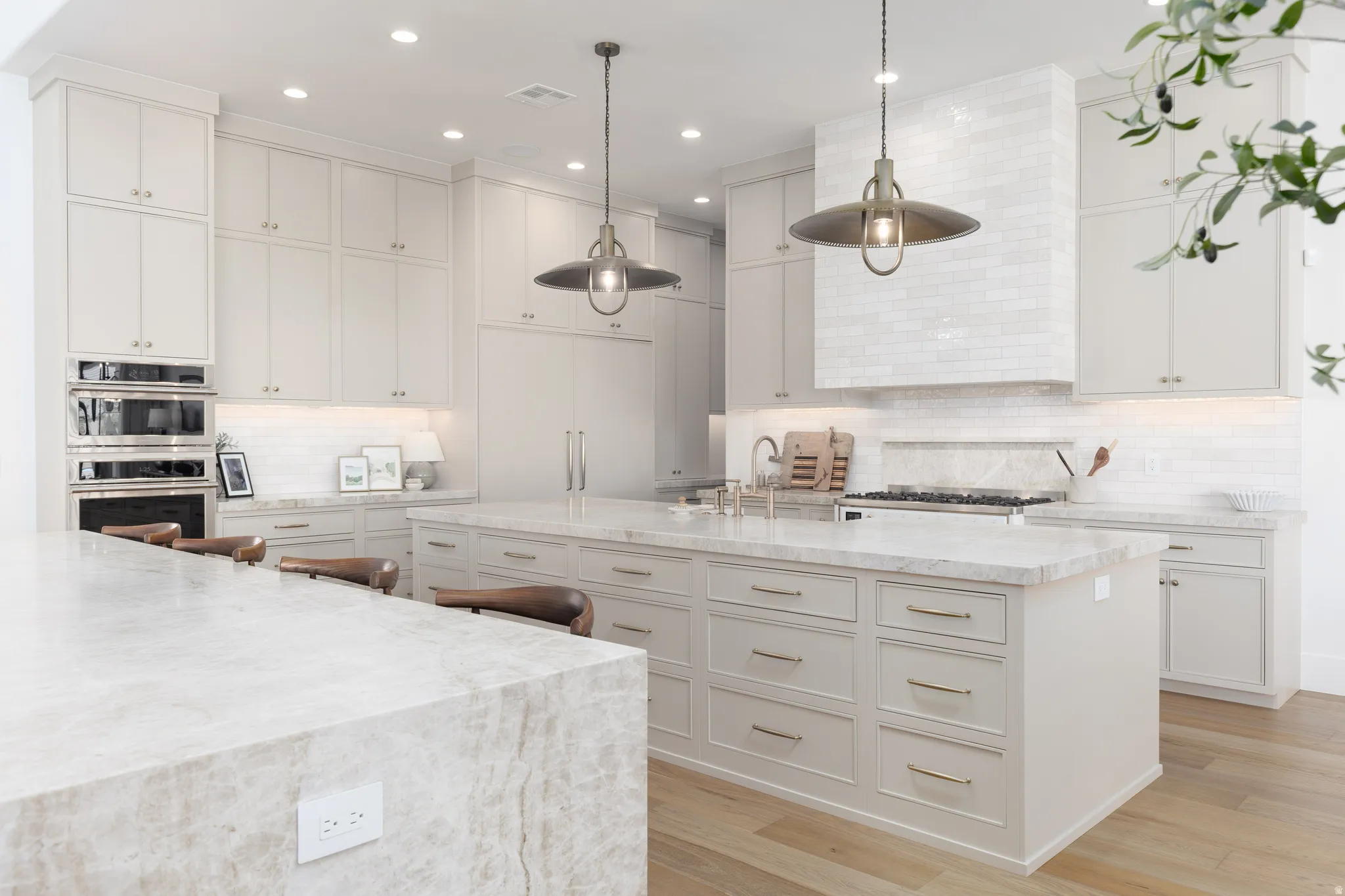 Kitchen with tasteful backsplash, pendant lighting, light stone countertops, light wood-style flooring, and stainless steel double oven