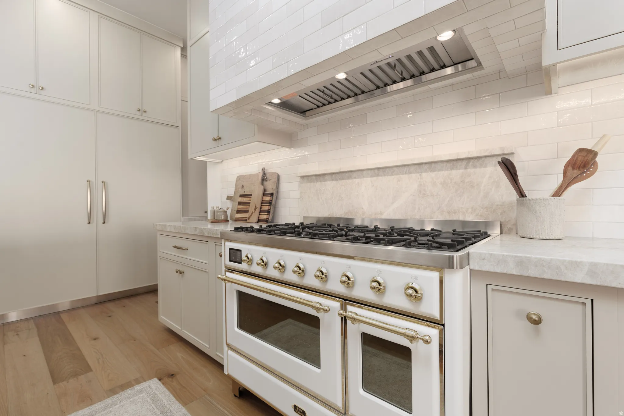 Kitchen featuring double oven range, light wood-style flooring, white cabinetry, light stone counters, and tasteful backsplash