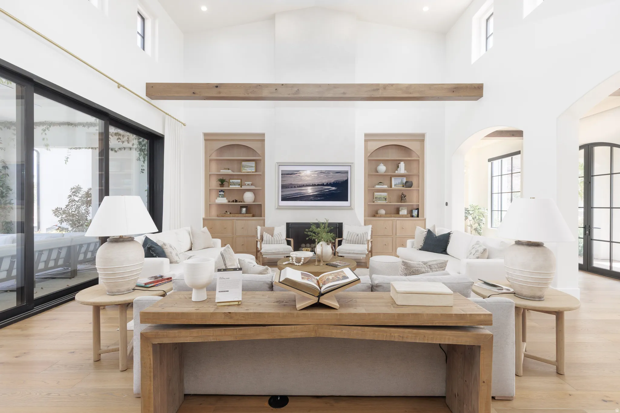 Living area with arched walkways, light wood finished floors, built in shelves, recessed lighting, and vaulted ceiling