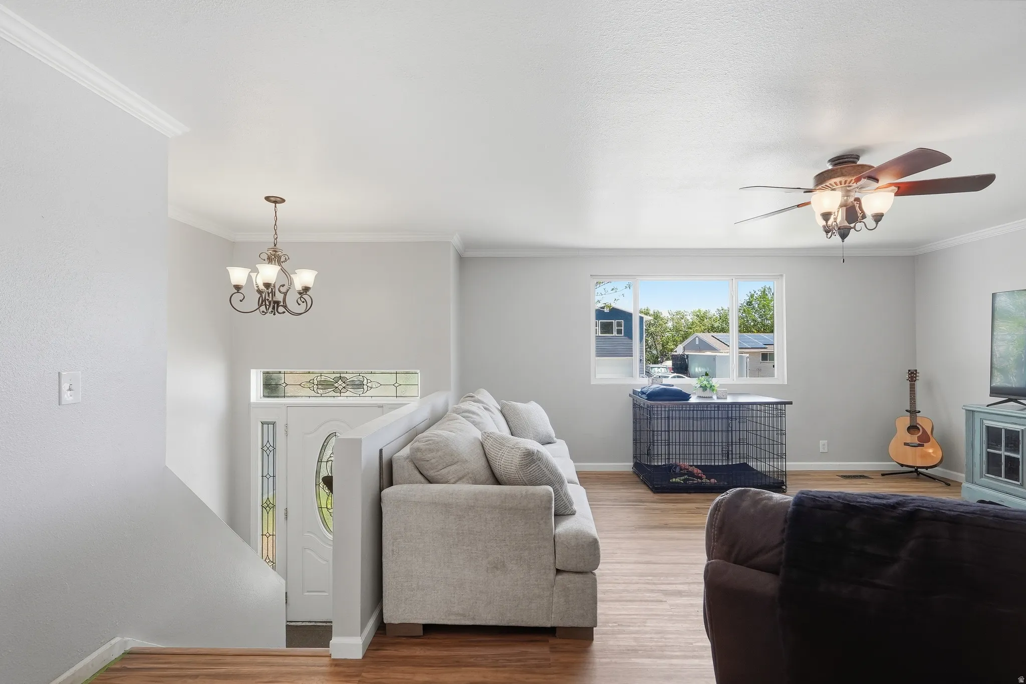 Bright living area featuring wood-finish flooring, white crown molding, and a ceiling fan with integrated lighting