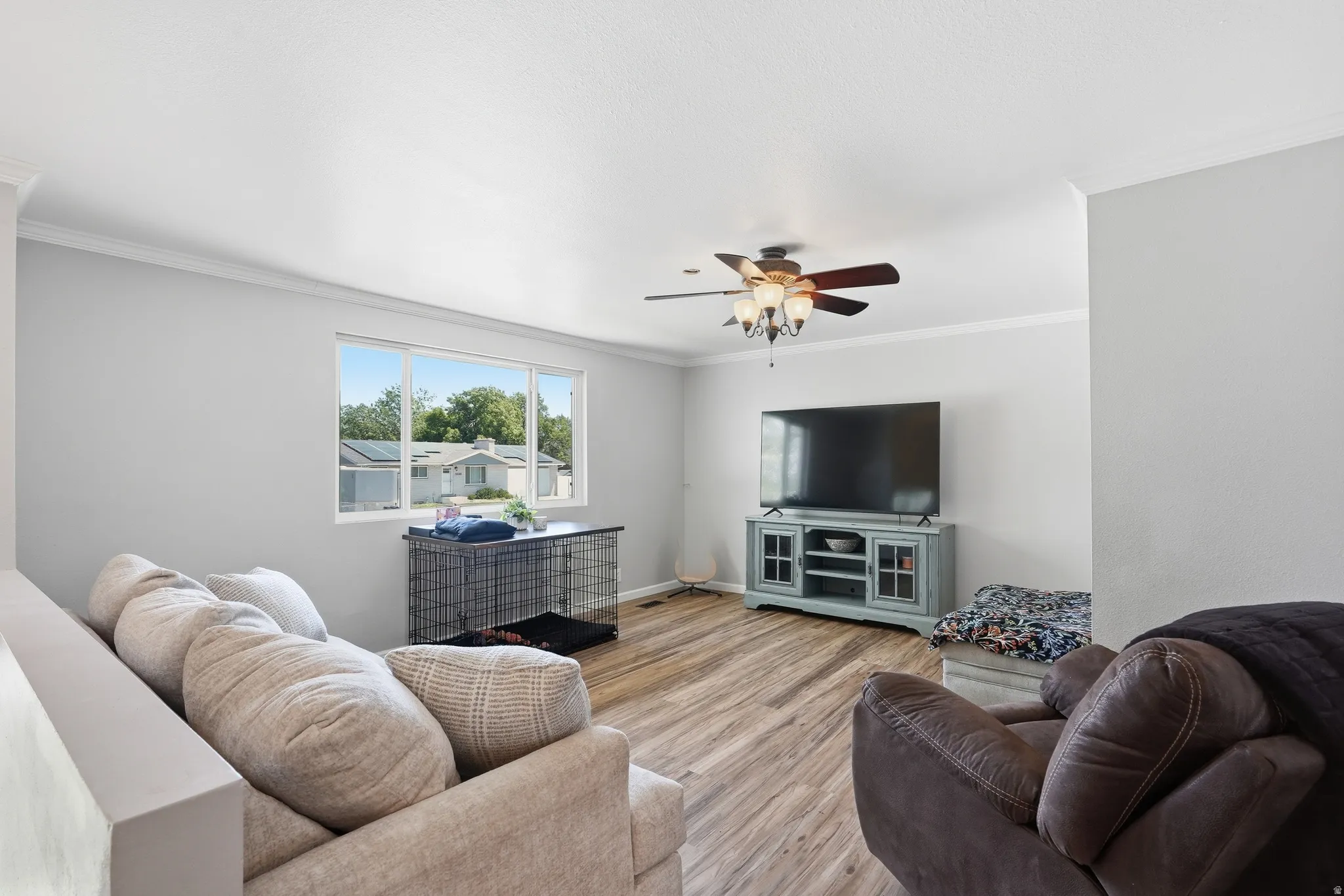 Light-filled living area featuring wood-finish flooring, a contemporary ceiling fan with integrated lighting, and crown molding accents