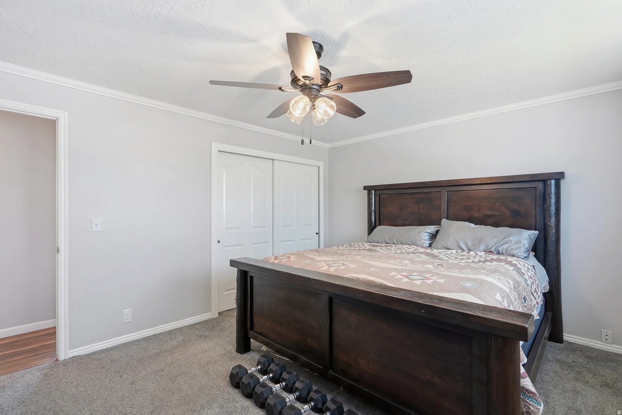 Carpeted room featuring a ceiling fan with integrated lighting, white baseboards, crown molding, and a sliding two-panel closet door