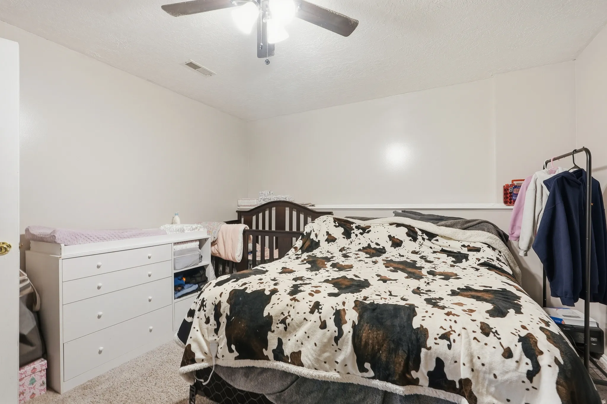White painted walls with a textured ceiling, neutral carpet, and a ceiling fan with light fixture