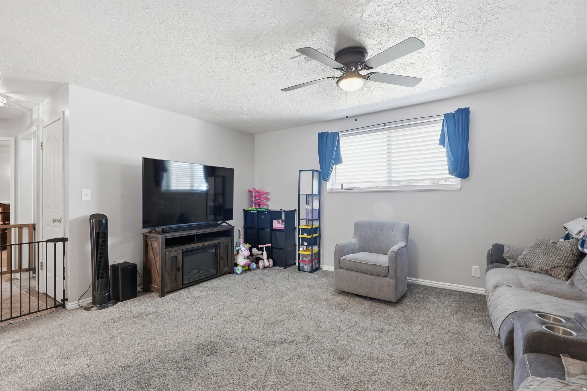 Carpeted living area featuring light gray walls and a ceiling fan with integrated lighting