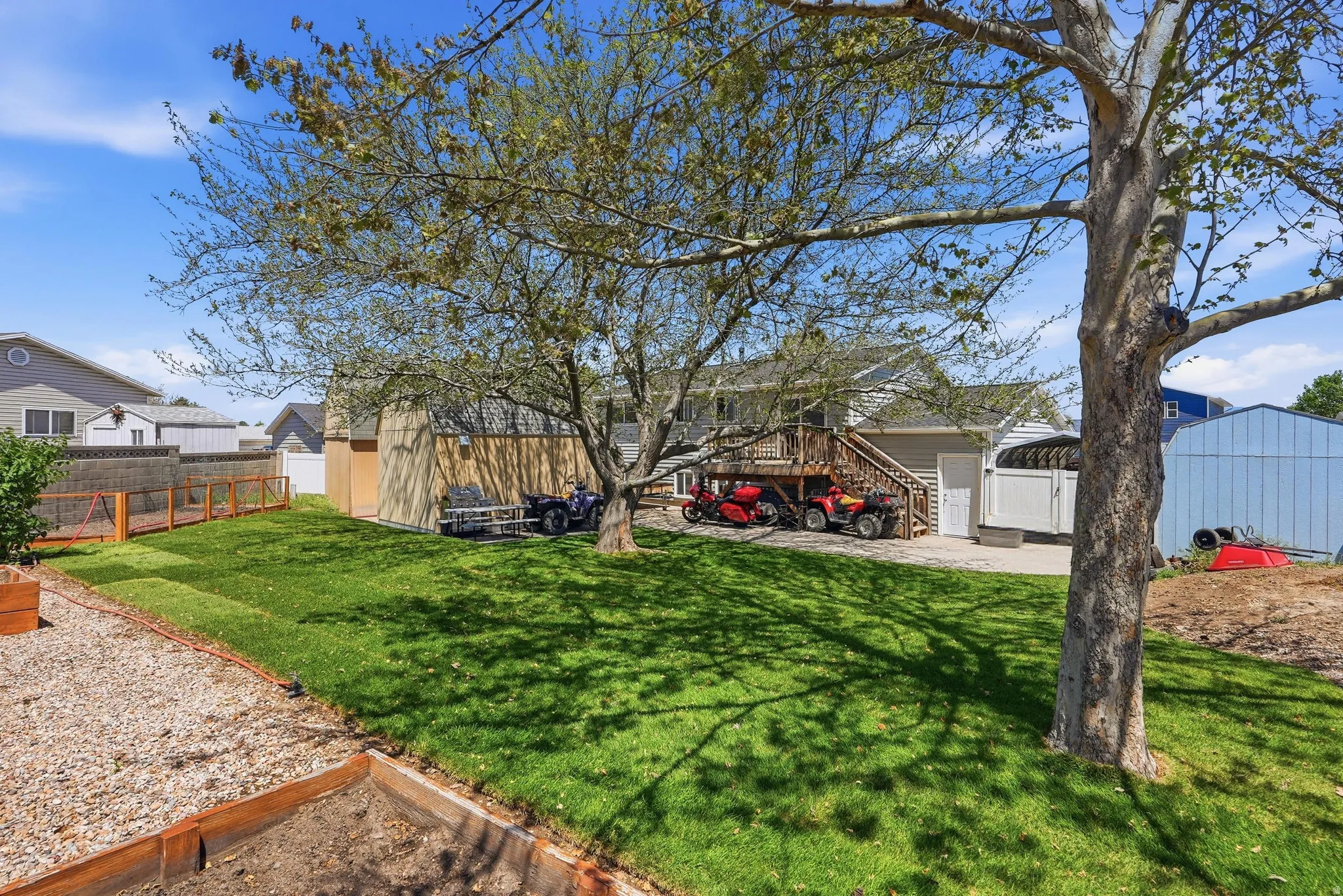 Spacious backyard featuring a manicured lawn, mature trees, and a raised garden bed