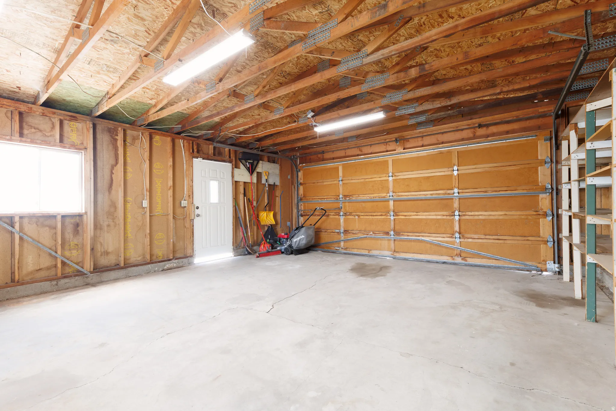 Attached garage interior featuring a concrete floor, exposed wood ceiling joists, and fluorescent lighting