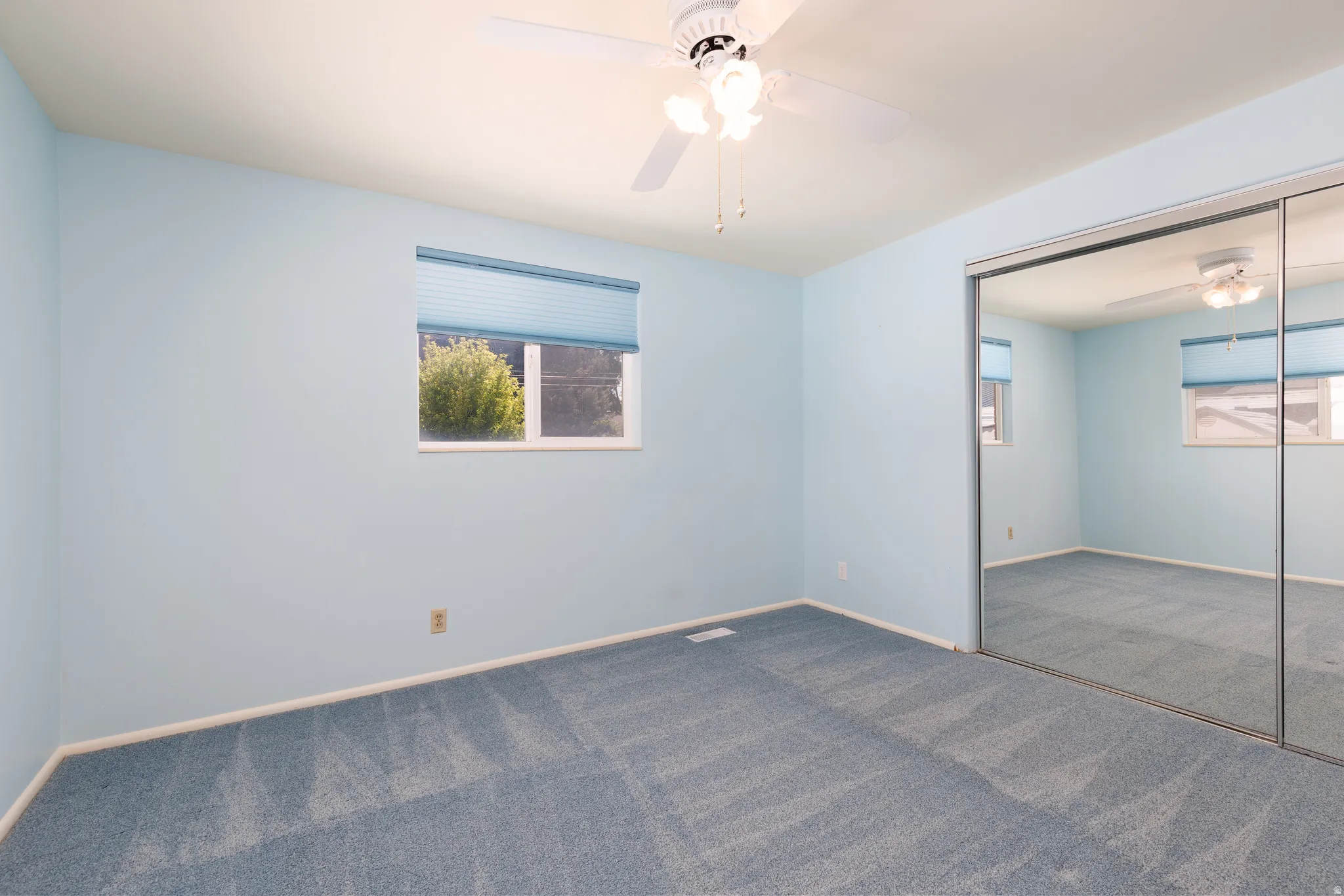 Primary bedroom featuring wall-to-wall carpeting, a window with cellular blinds, a ceiling fan with integrated lighting, and mirrored closet doors