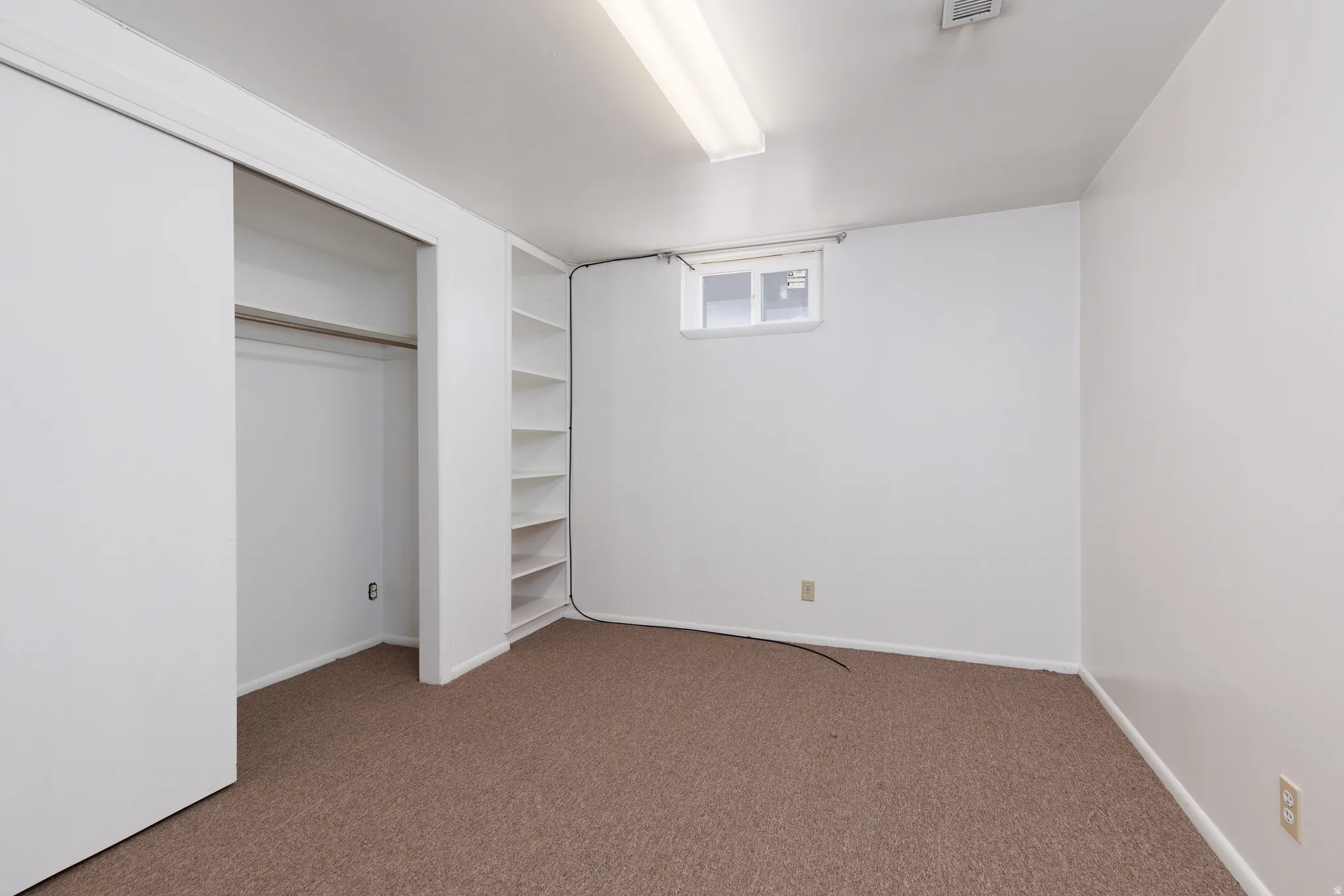 Versatile room featuring brown carpet flooring, white walls, and a white built-in shelving unit