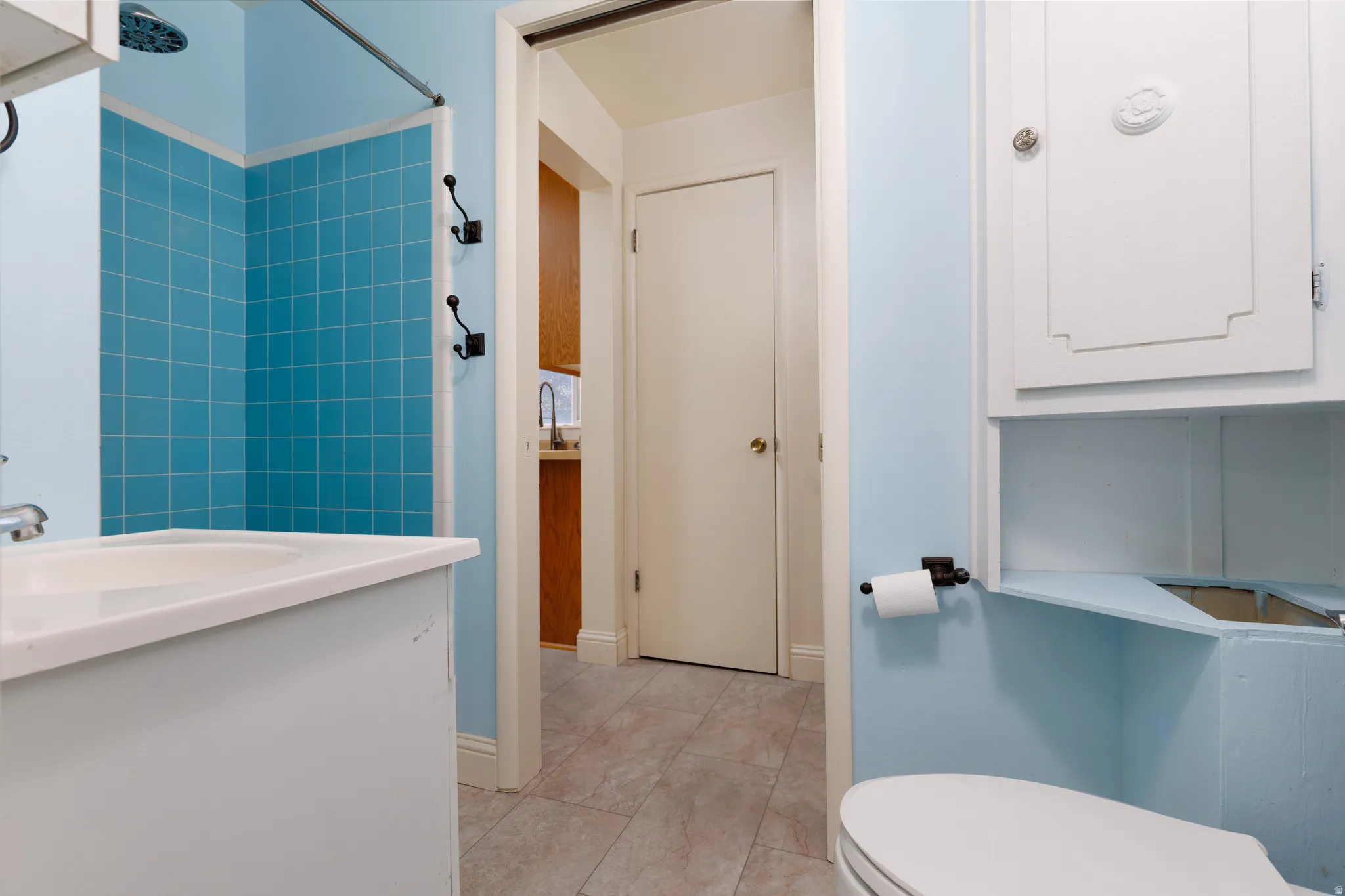 Primary Bathroom featuring a white vanity with integrated sink, a tiled shower with blue square tiles, an overhead showerhead, and a built-in white medicine cabinet