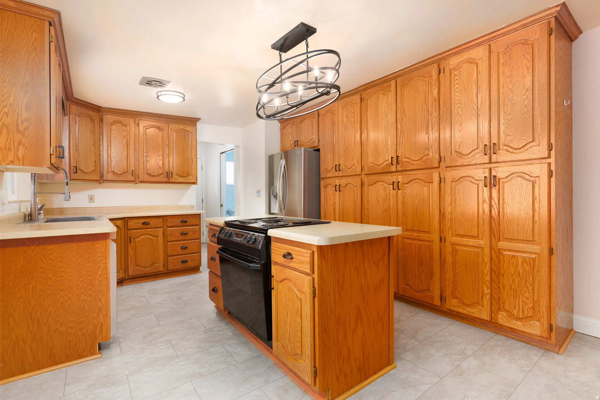 Kitchen featuring extensive wood cabinetry, a central island with a built-in electric range, stainless steel refrigerator, and light-toned countertops