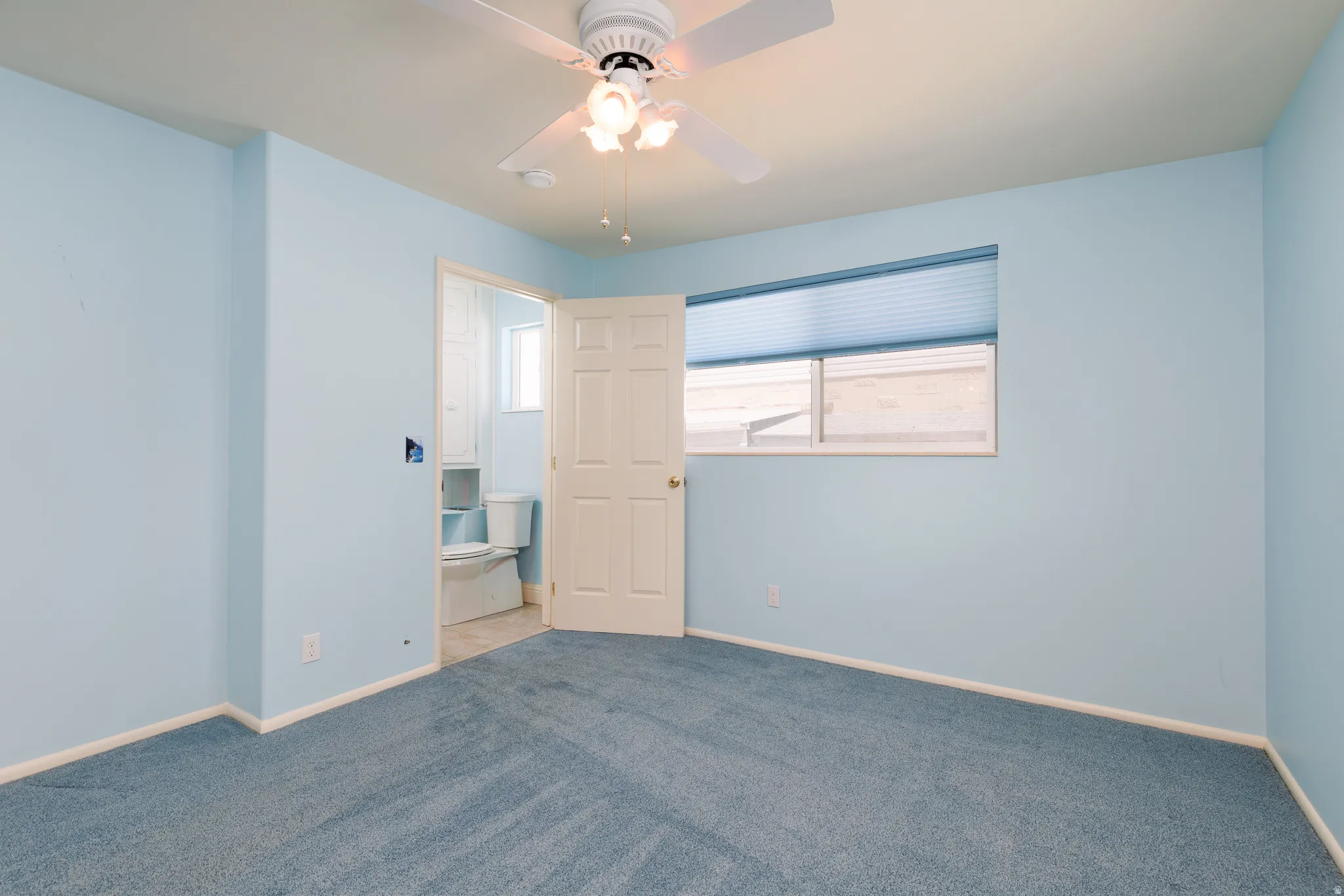 Primary bedroom with blue carpeting and light blue walls, featuring a ceiling fan with integrated lighting