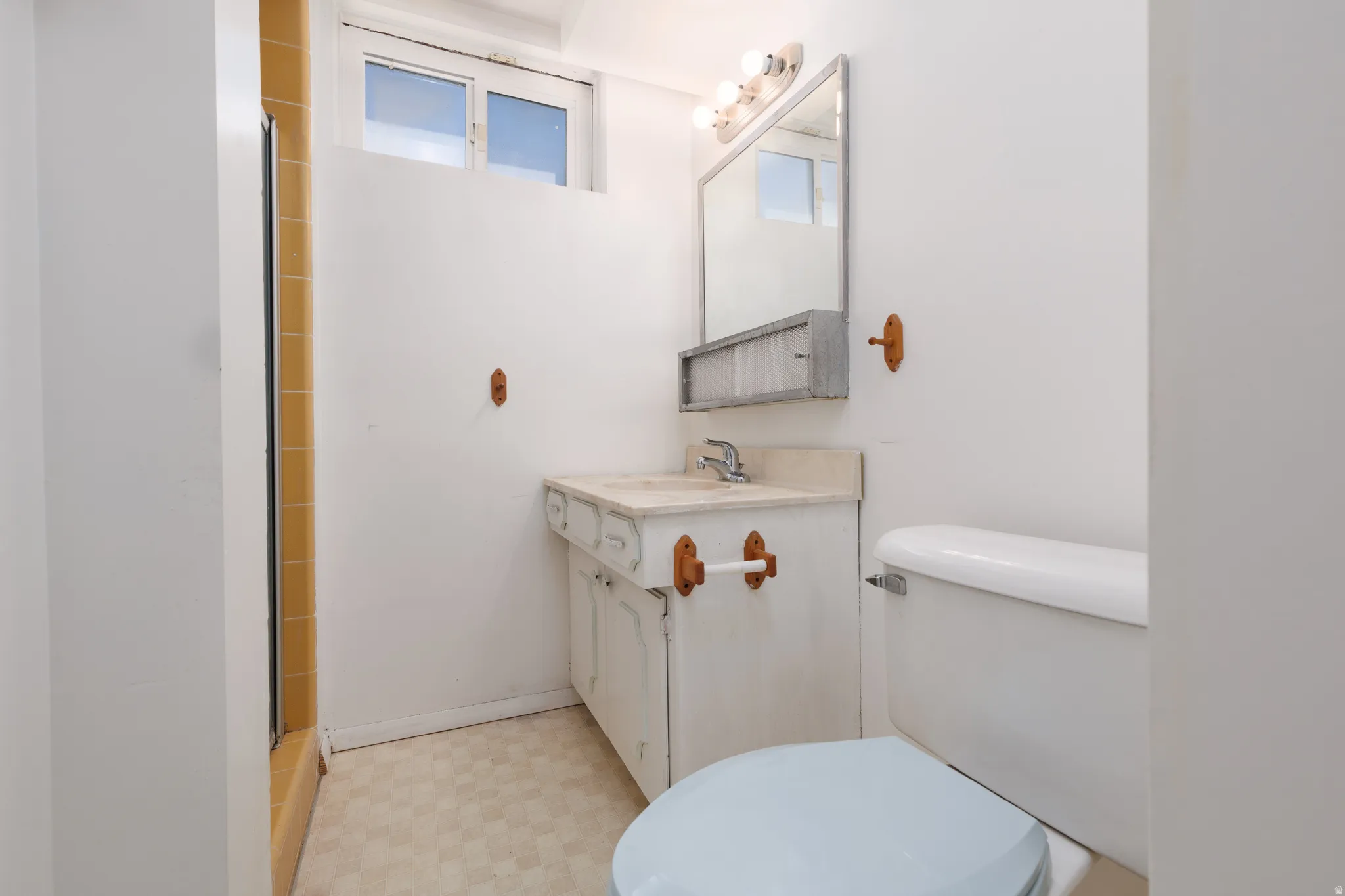 Bathroom featuring a white vanity with integrated sink, patterned floor tiles, and a window above the shower