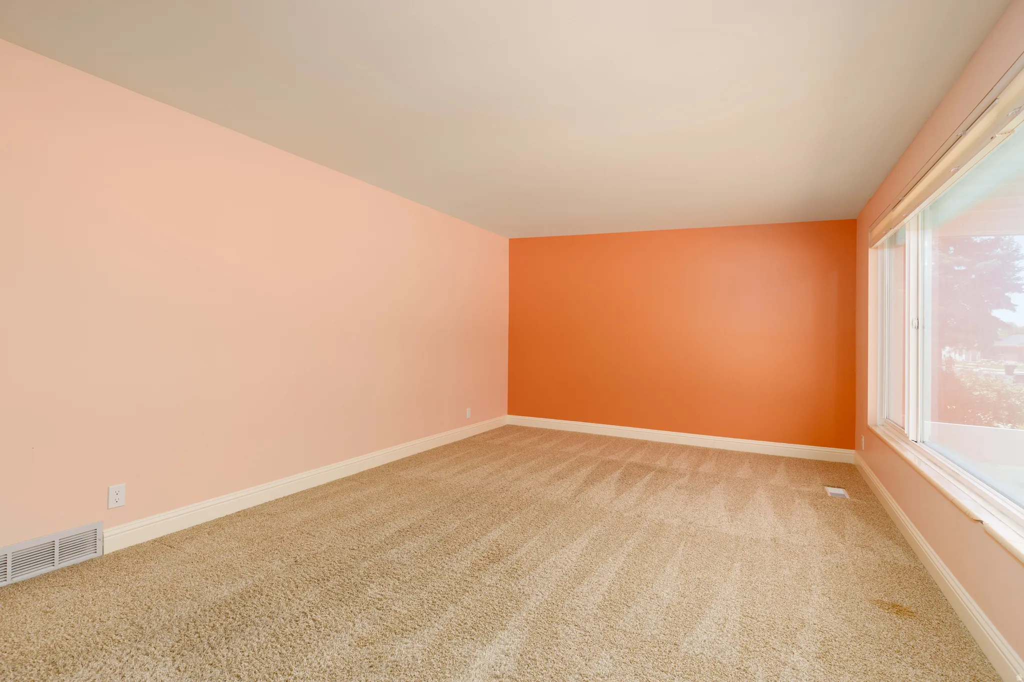 Spacious interior room featuring carpet flooring, a large window, a light orange accent wall, and light peach walls