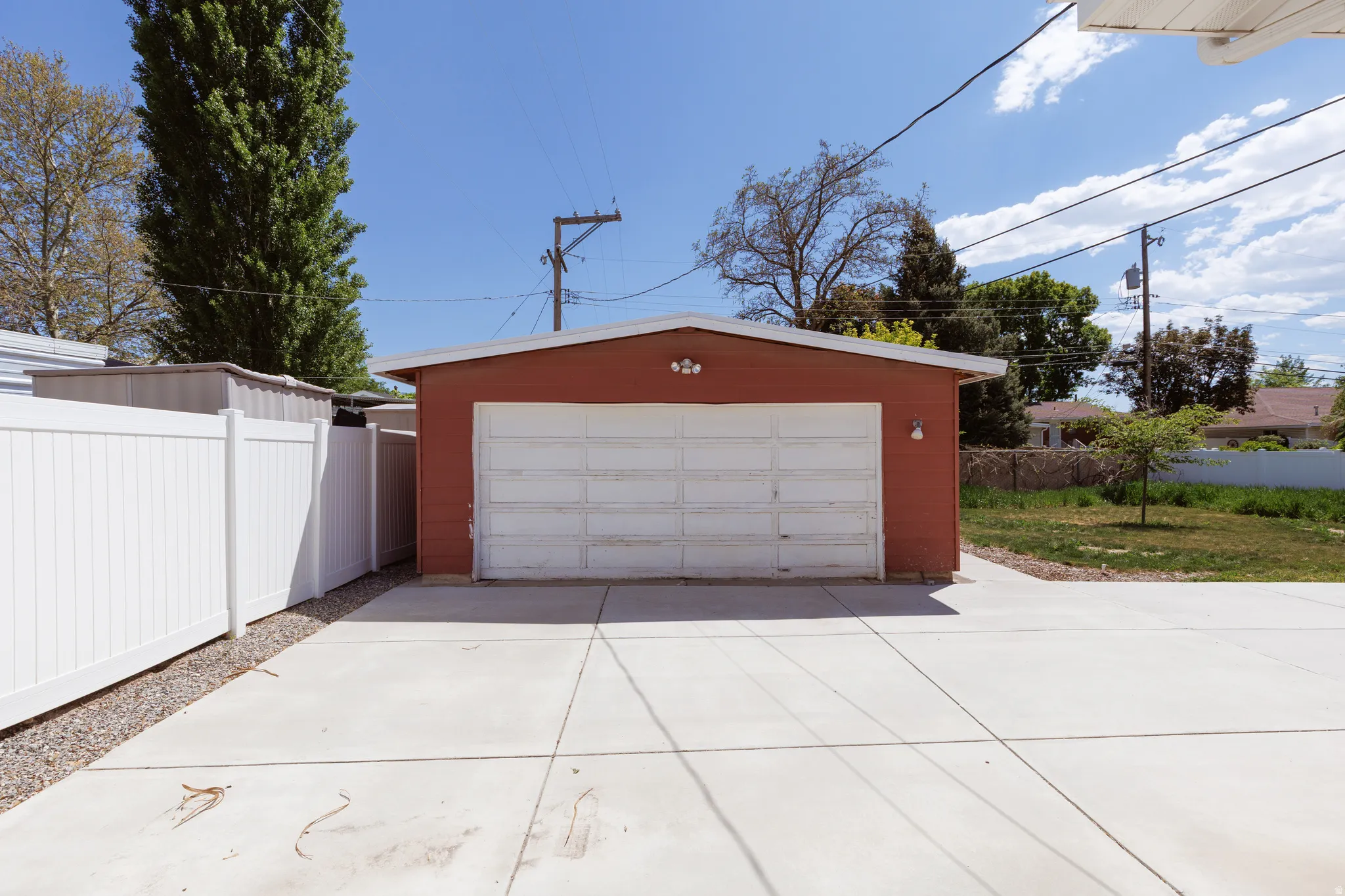 Detached garage with red siding, a white garage door, and a concrete driveway