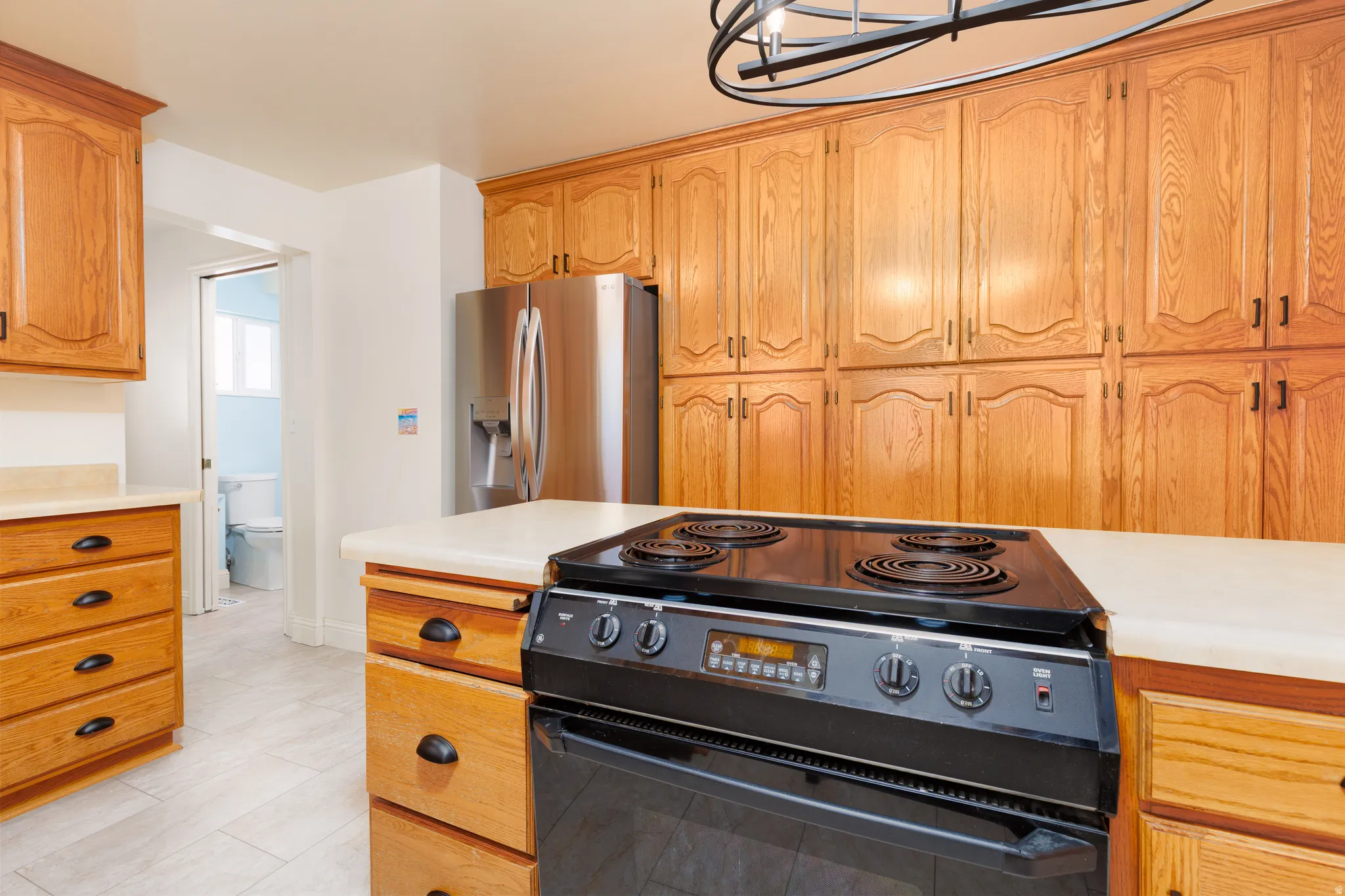 Kitchen featuring extensive natural wood cabinetry, light-toned countertops, tile flooring, and a stainless steel refrigerator