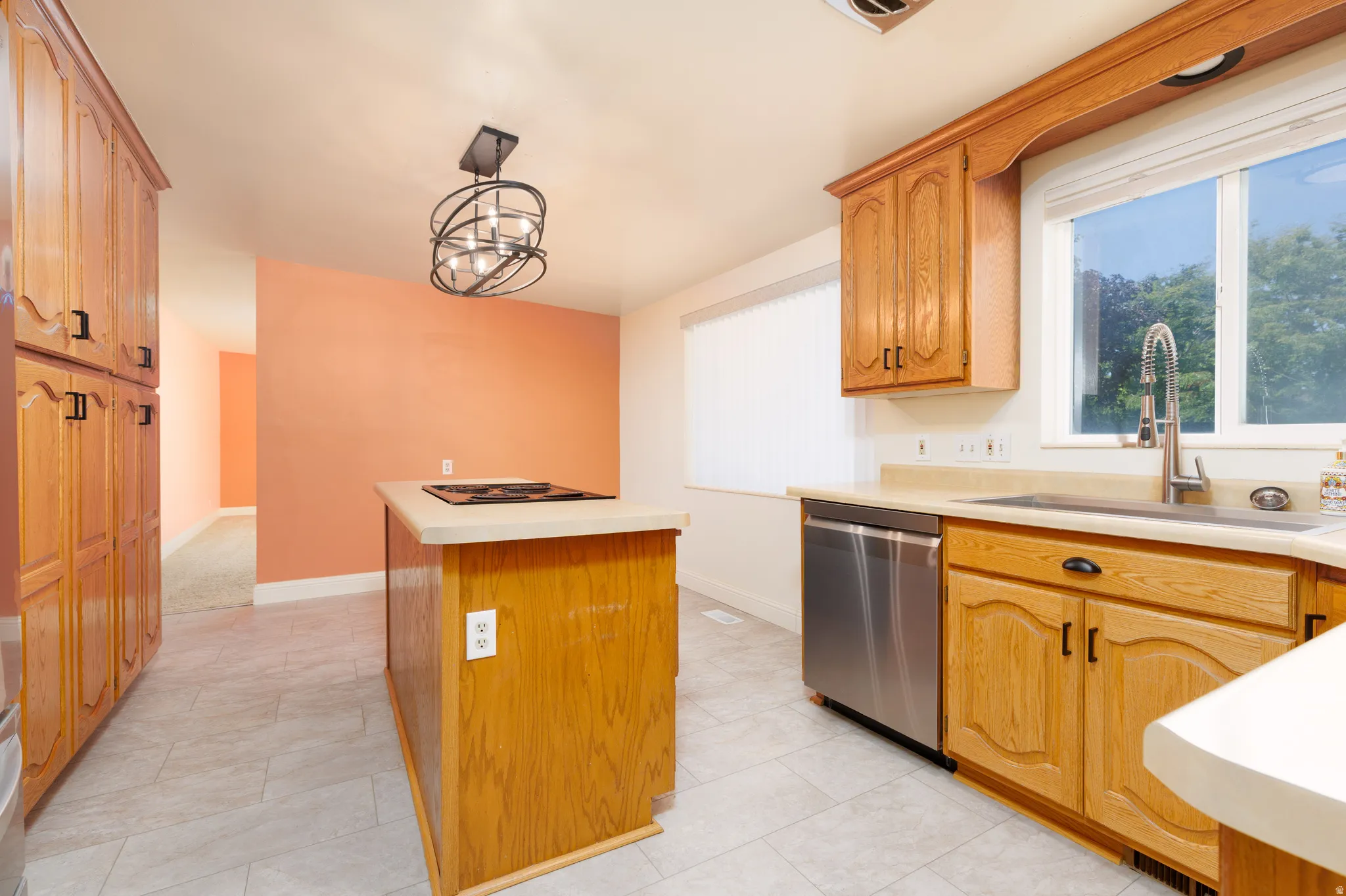 Kitchen featuring light wood cabinetry, a central island with an integrated cooktop, stainless steel dishwasher, a single basin sink with a gooseneck faucet, and tile flooring