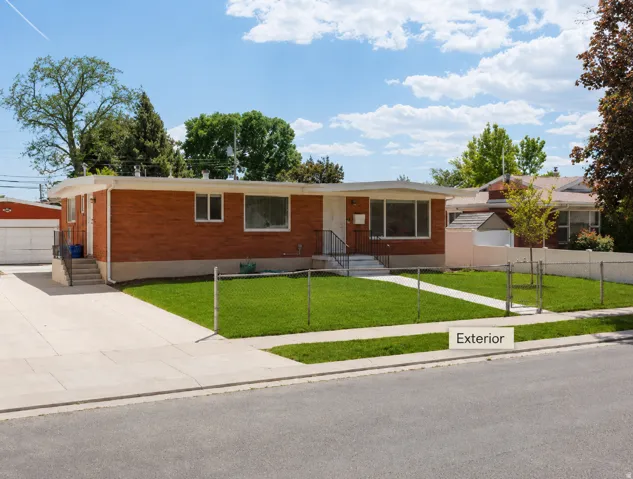 Brick exterior with a white trim roofline, mature trees, a manicured lawn, a concrete driveway, and a front walkway