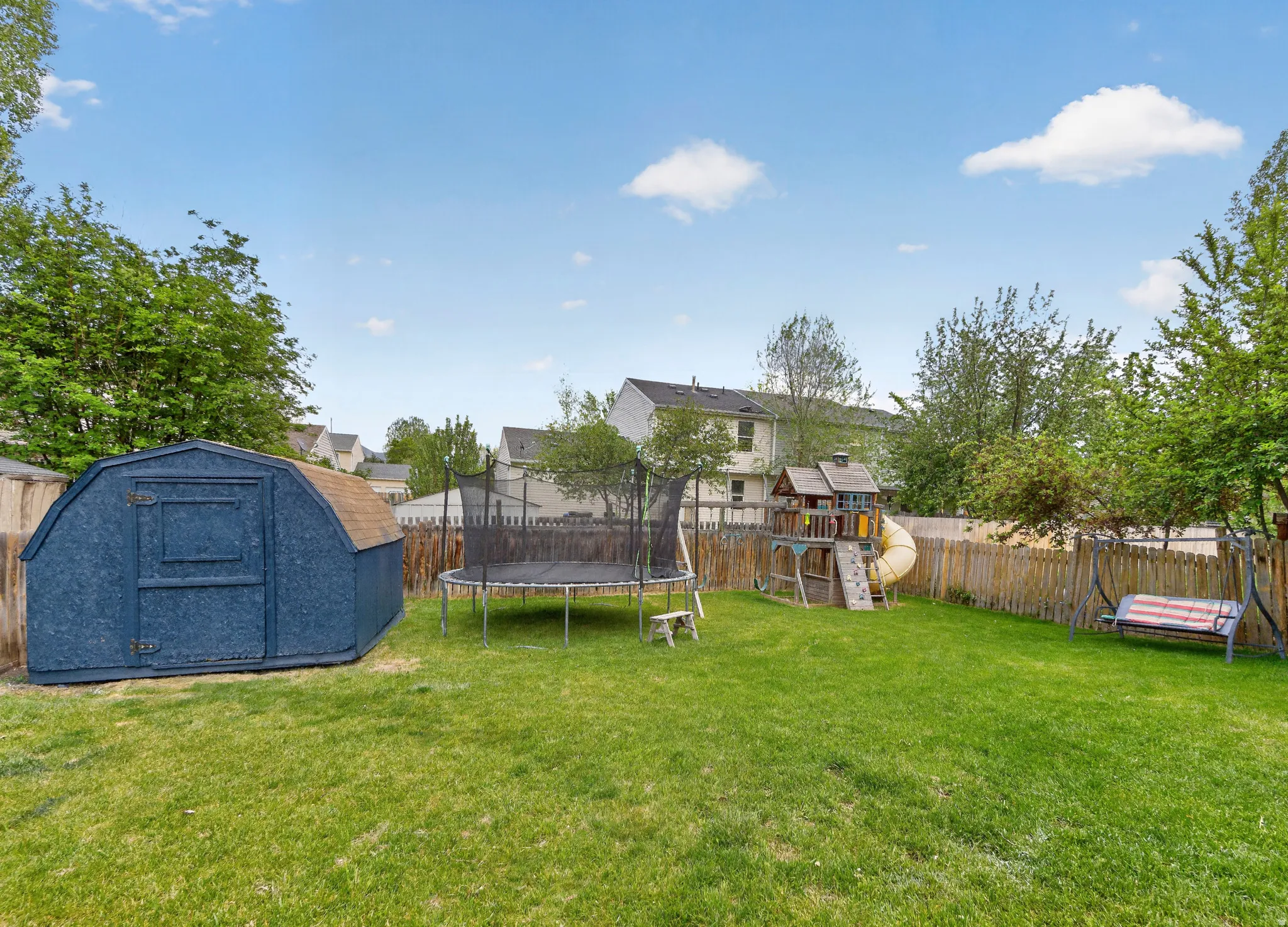 Spacious backyard featuring a manicured lawn, full perimeter wood fencing, and mature trees