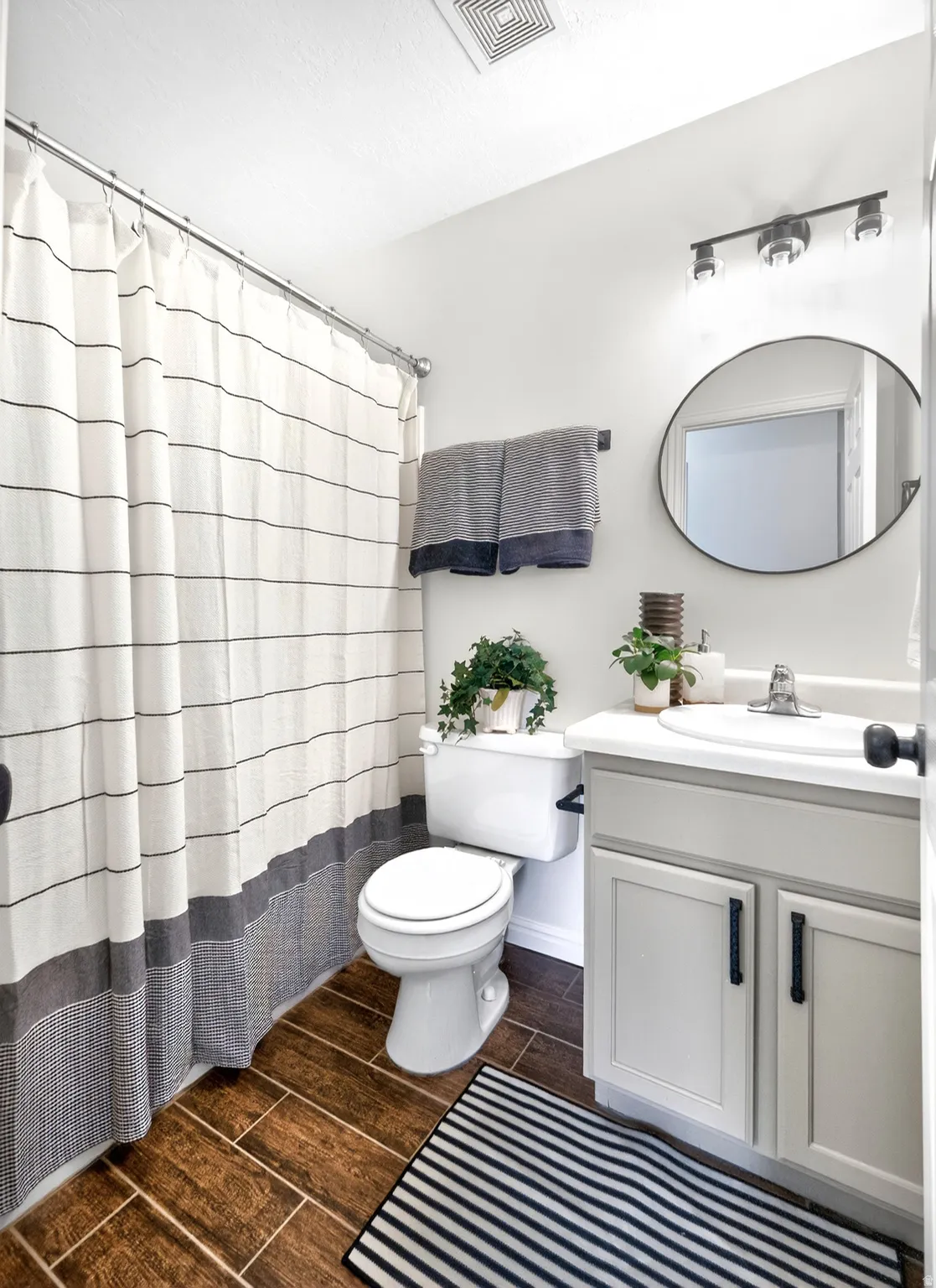 Bathroom featuring wood-look tile flooring, a white vanity with a single sink, an oval mirror, and a track light fixture