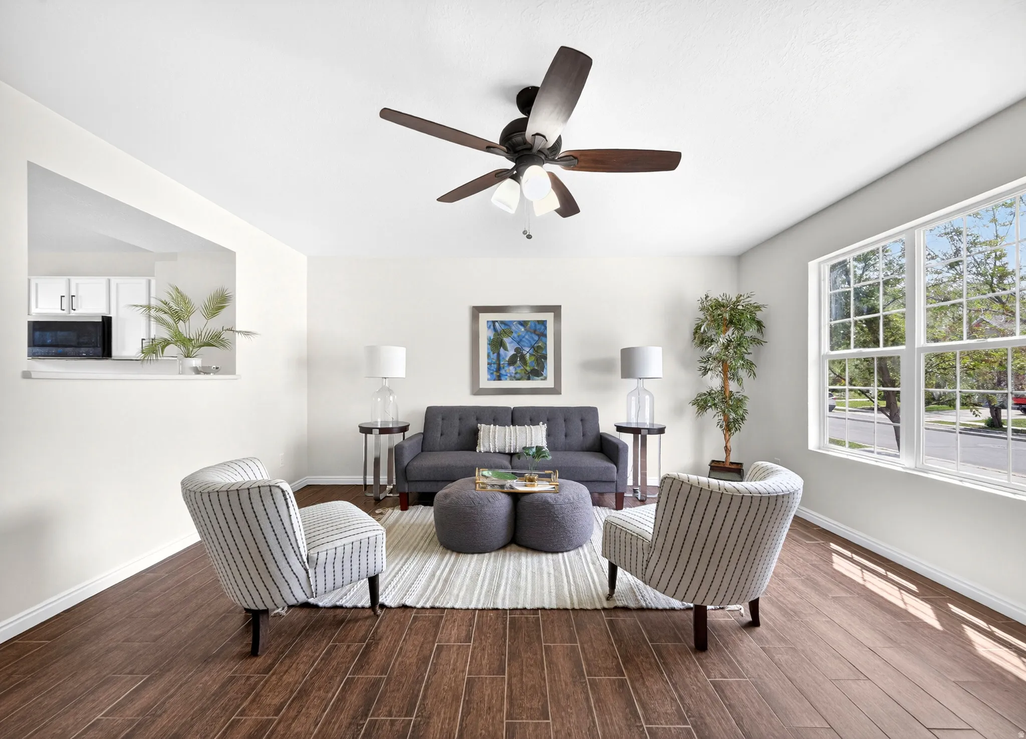 Spacious living area featuring wood-finish flooring, a contemporary ceiling fan, and large windows providing ample natural light