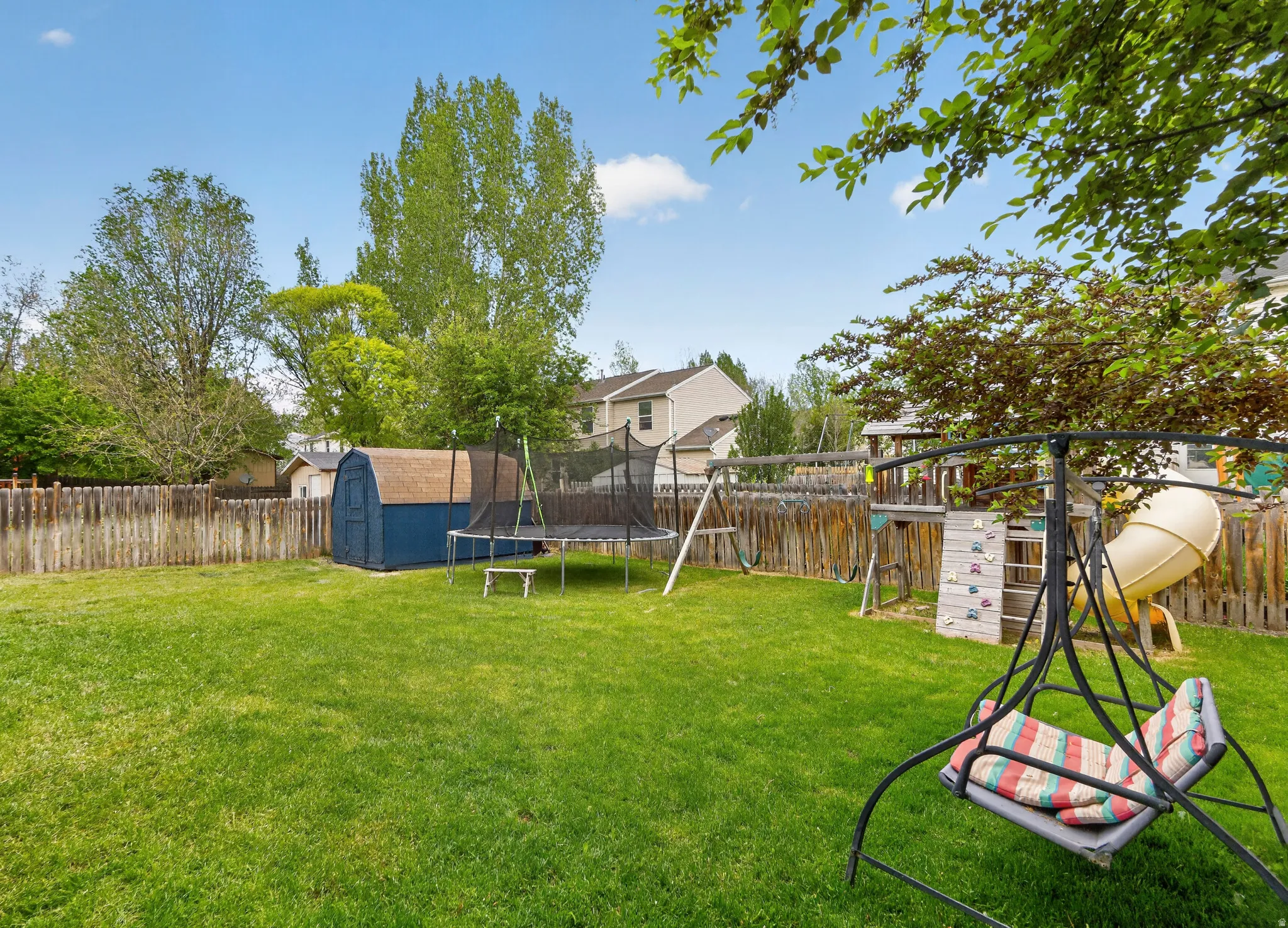 Expansive fenced backyard featuring a manicured lawn, mature trees, a blue storage shed, and a wooden privacy fence