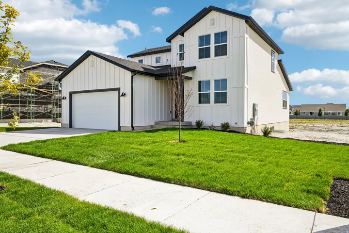 Contemporary two-story exterior with white board and batten siding, dark trim, an attached garage, and a manicured lawn