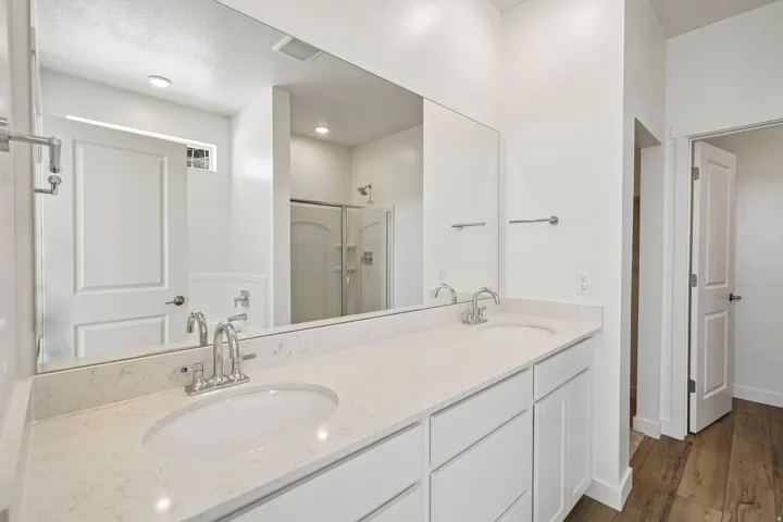 Dual basin vanity with stone countertop, wood-finish flooring, recessed lighting, and a shower with a sliding glass enclosure