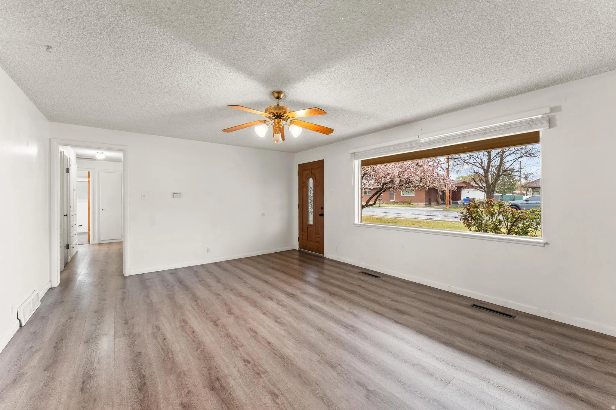 Unfurnished living room featuring light wood-style floors, a ceiling fan, and a textured ceiling