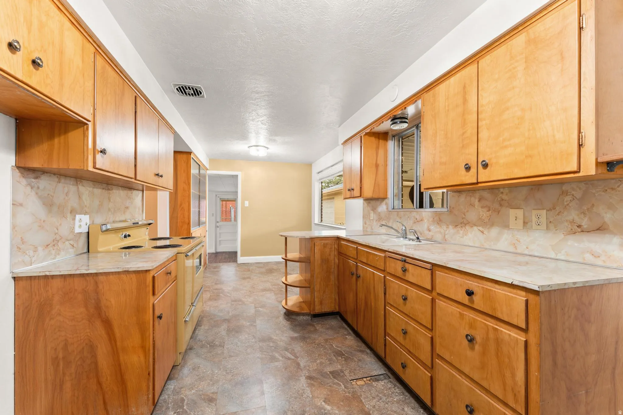 Kitchen with light countertops, backsplash, double oven range, stone finish flooring, and a textured ceiling
