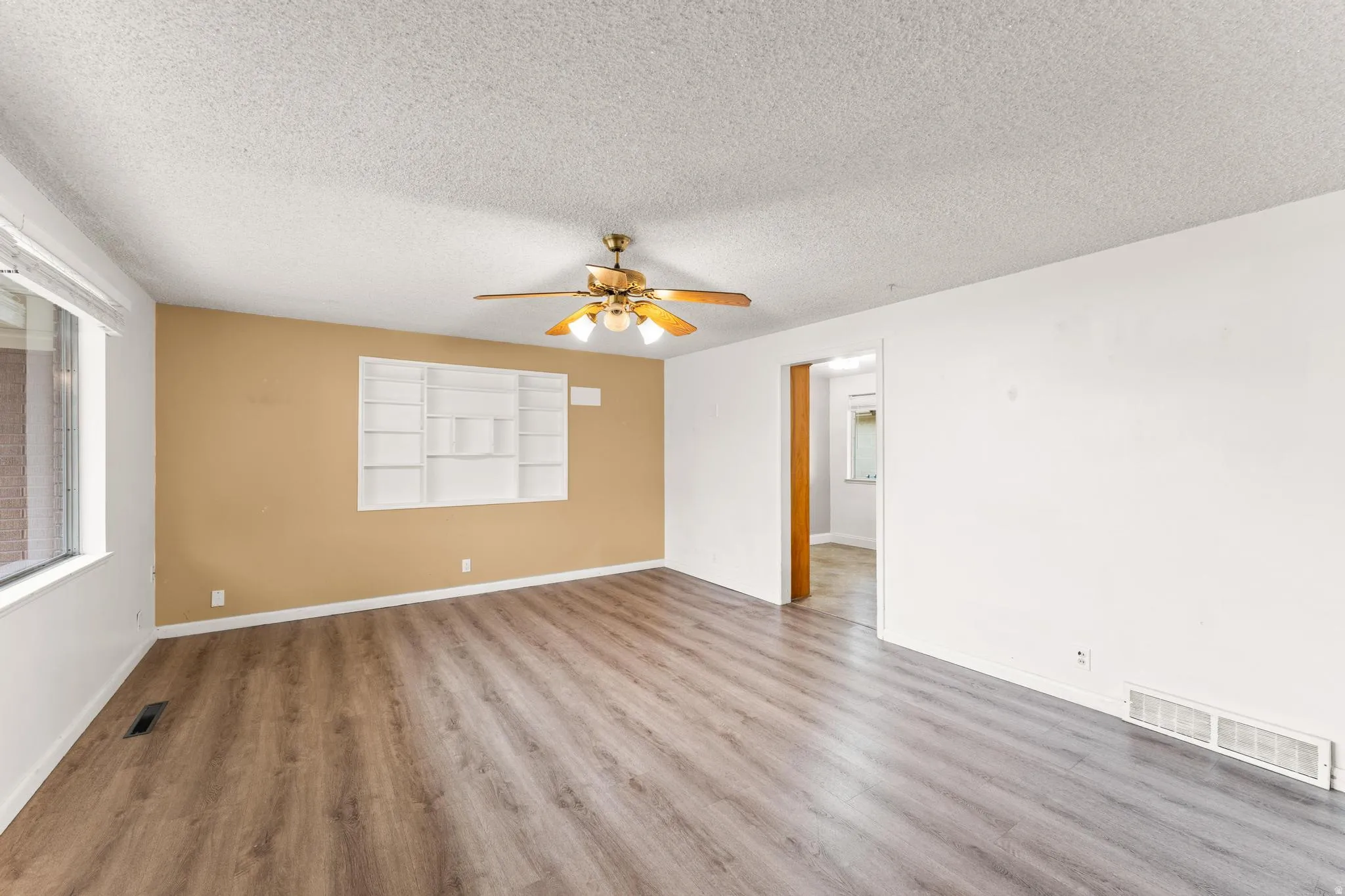 Unfurnished room featuring a ceiling fan, light wood-style flooring, and a textured ceiling