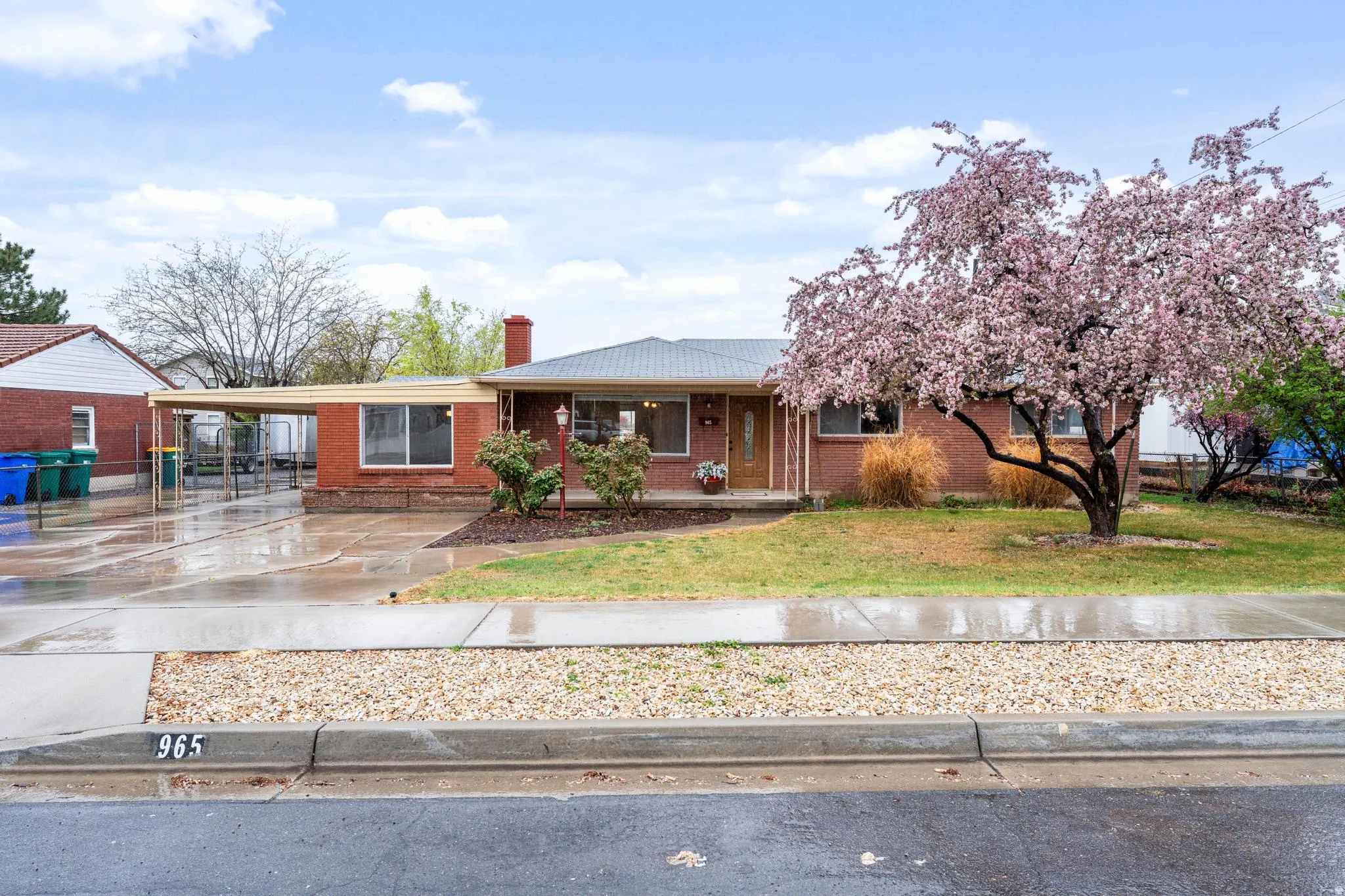 View of front of home with covered porch, driveway, an attached carport, a front lawn, and brick siding