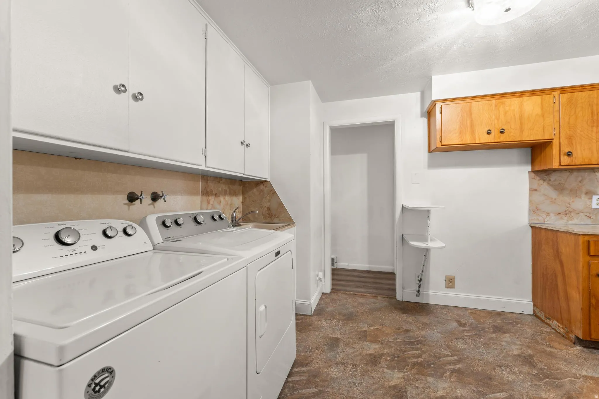 Laundry area featuring independent washer and dryer, a textured ceiling, and cabinet space