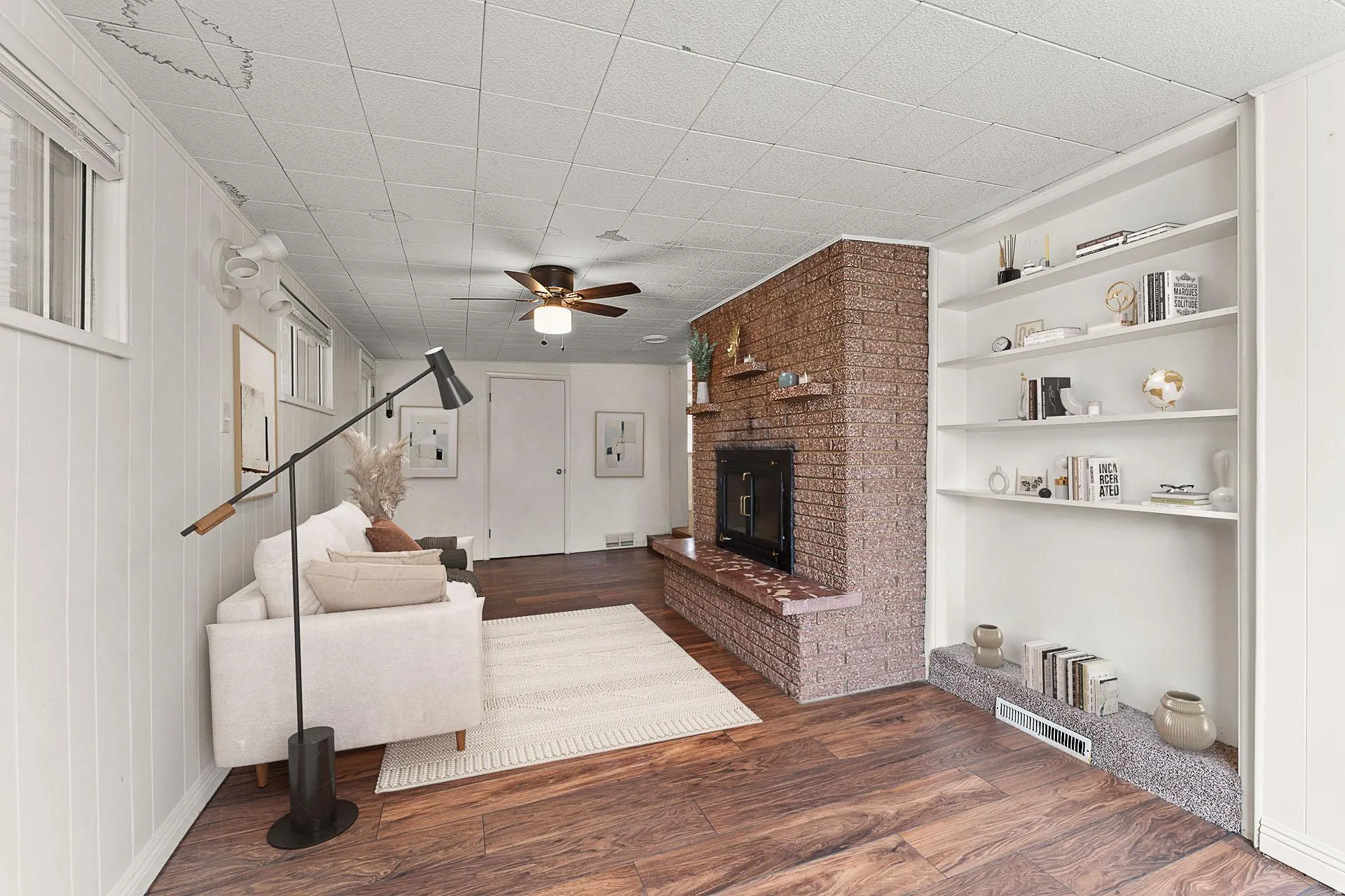 *Virtually Staged* Unfurnished living room featuring dark wood-style flooring, a brick fireplace, ceiling fan, and built in features