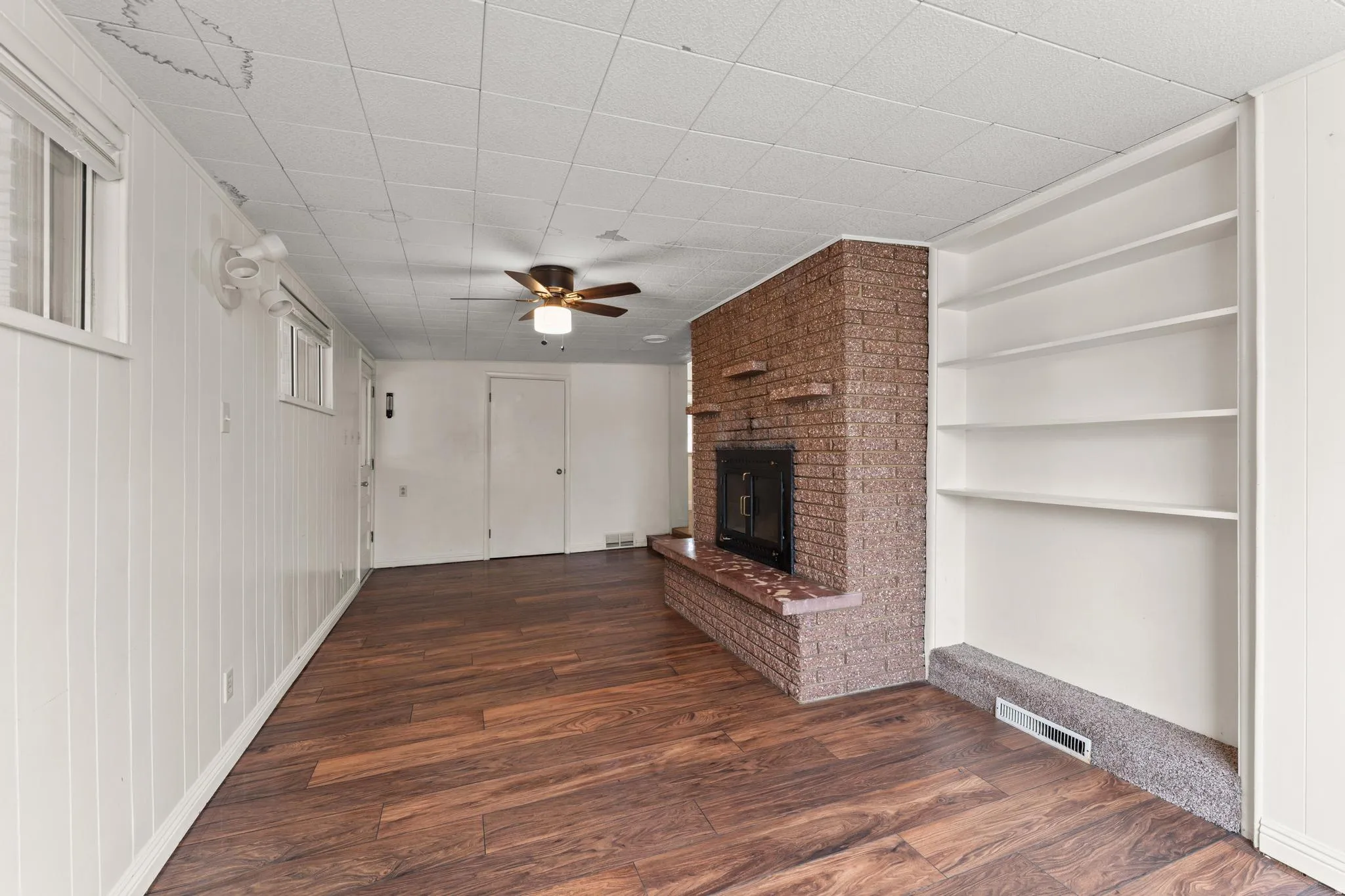 Unfurnished living room with dark wood finished floors, ceiling fan, a fireplace, and built in shelves