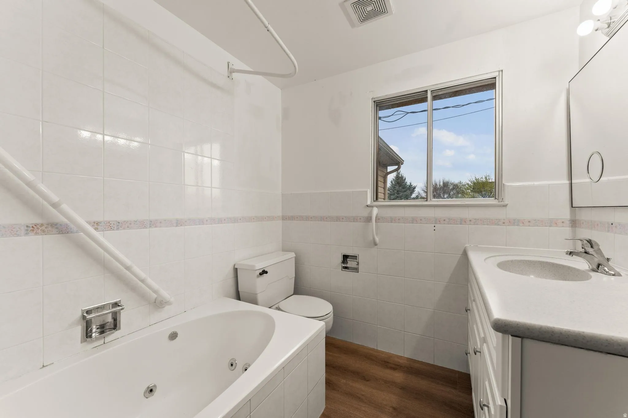 Bathroom with vanity, wainscoting, tile walls, dark wood-style floors, and a combined bath / shower with jetted tub
