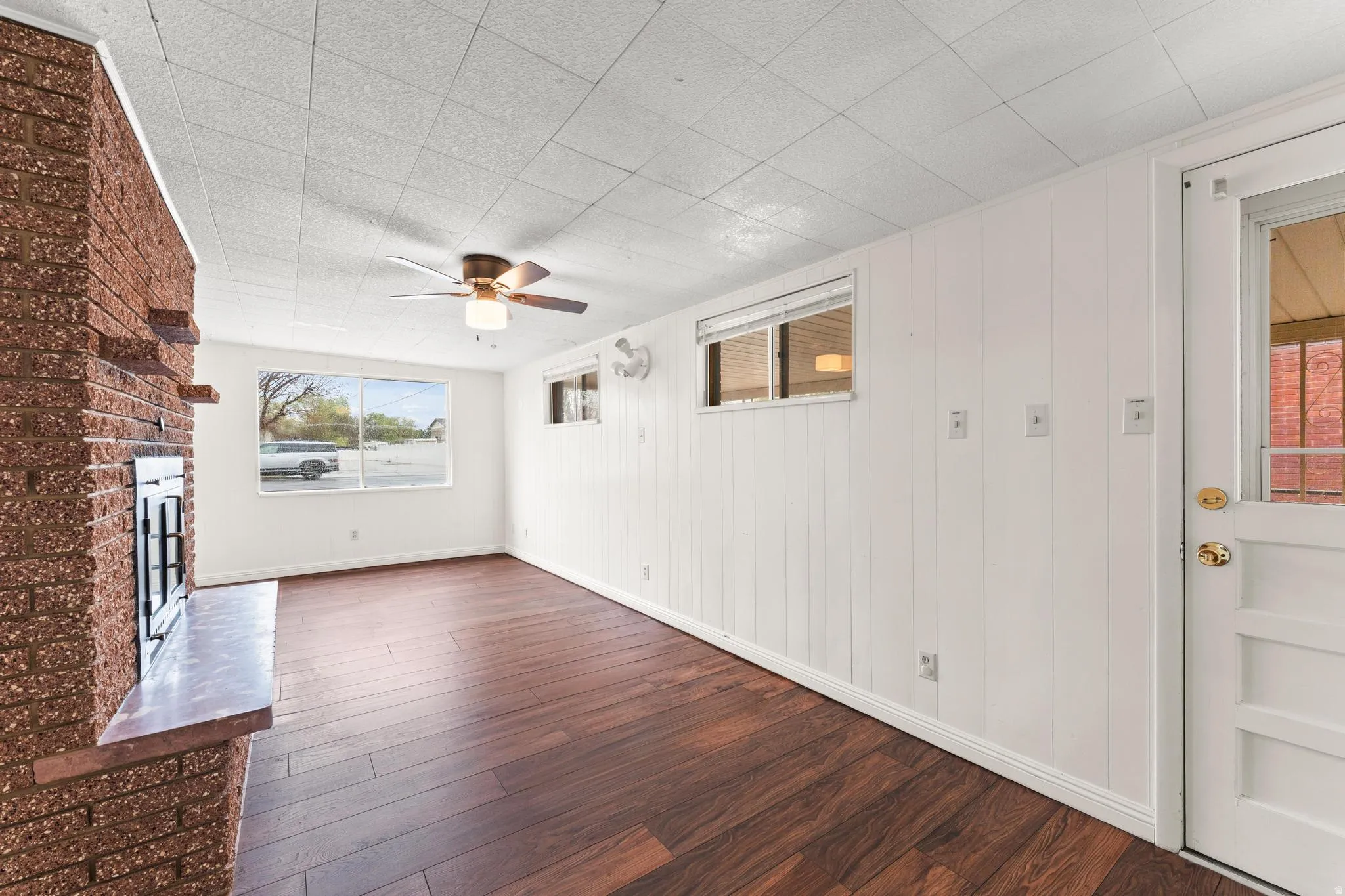 Unfurnished living room with dark wood-type flooring, a brick fireplace, and ceiling fan