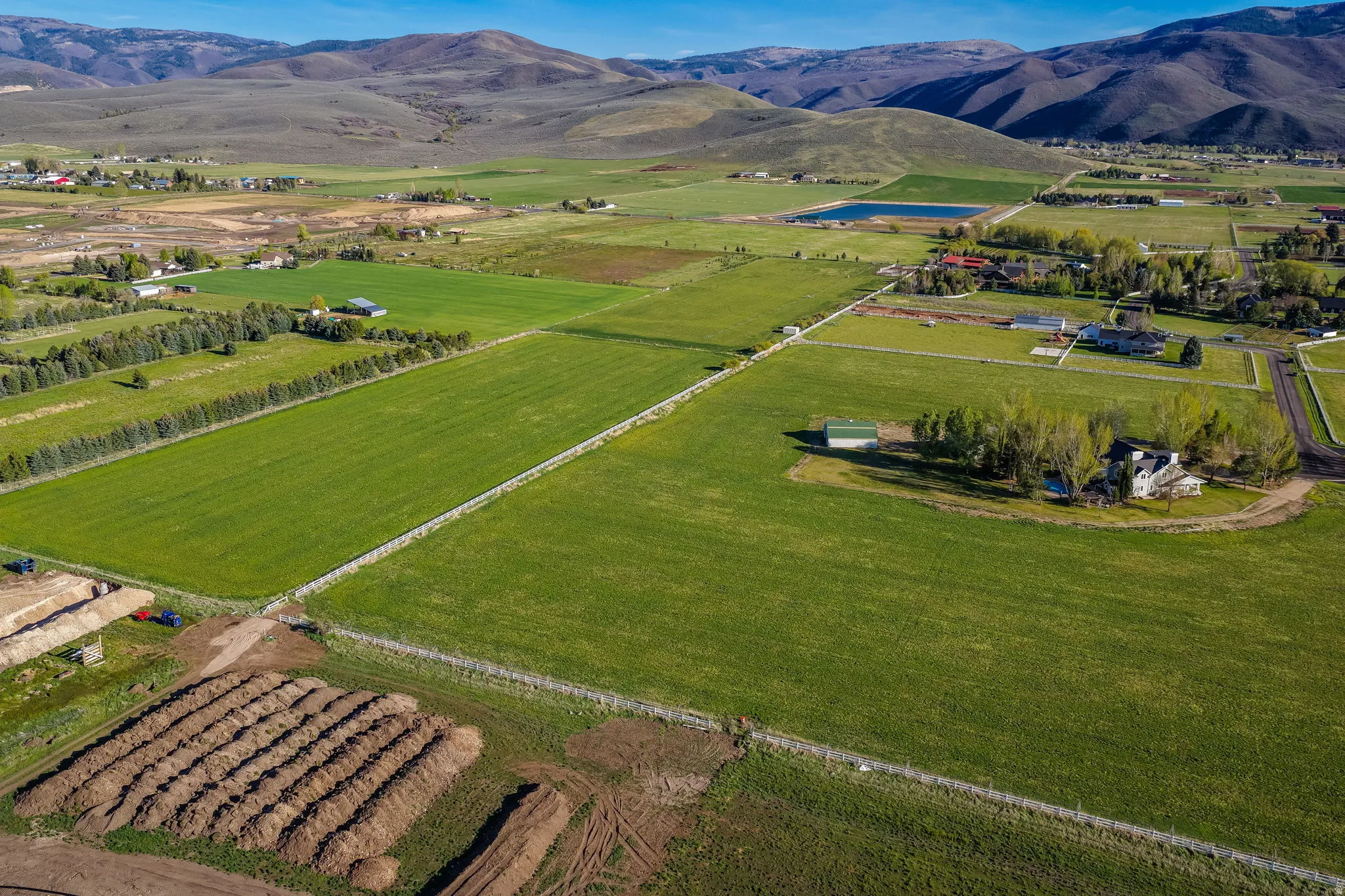 Expansive agricultural land featuring a verdant field, mountain backdrop, and multiple building sites