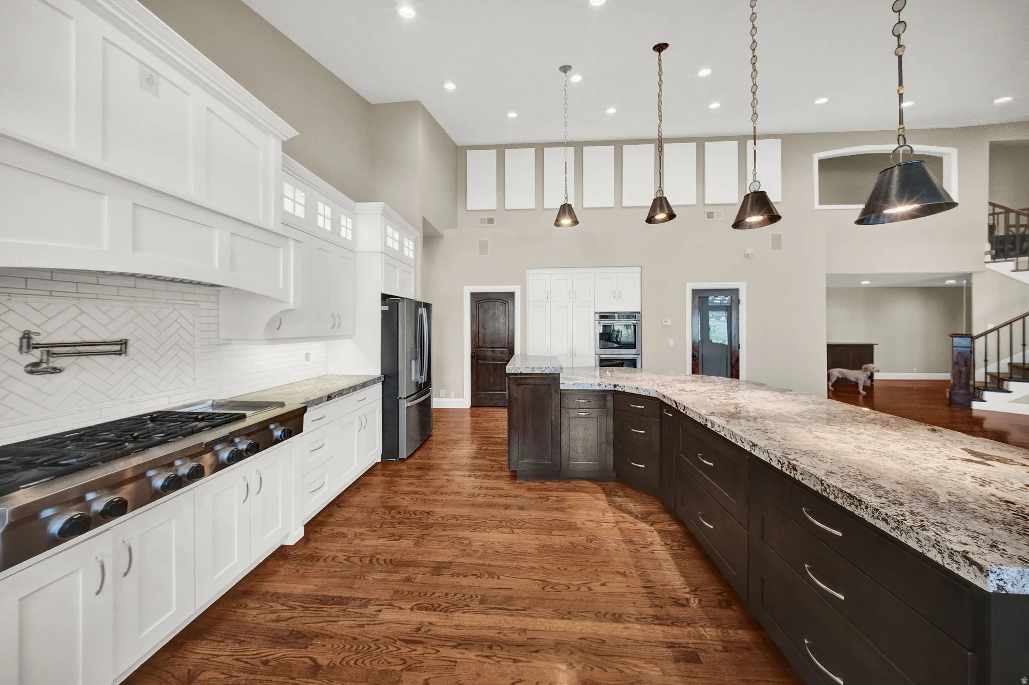 Spacious kitchen featuring an extended curved island with a stone-finish countertop, a stainless steel range with a pot filler, white shaker cabinetry, and wood-finish flooring