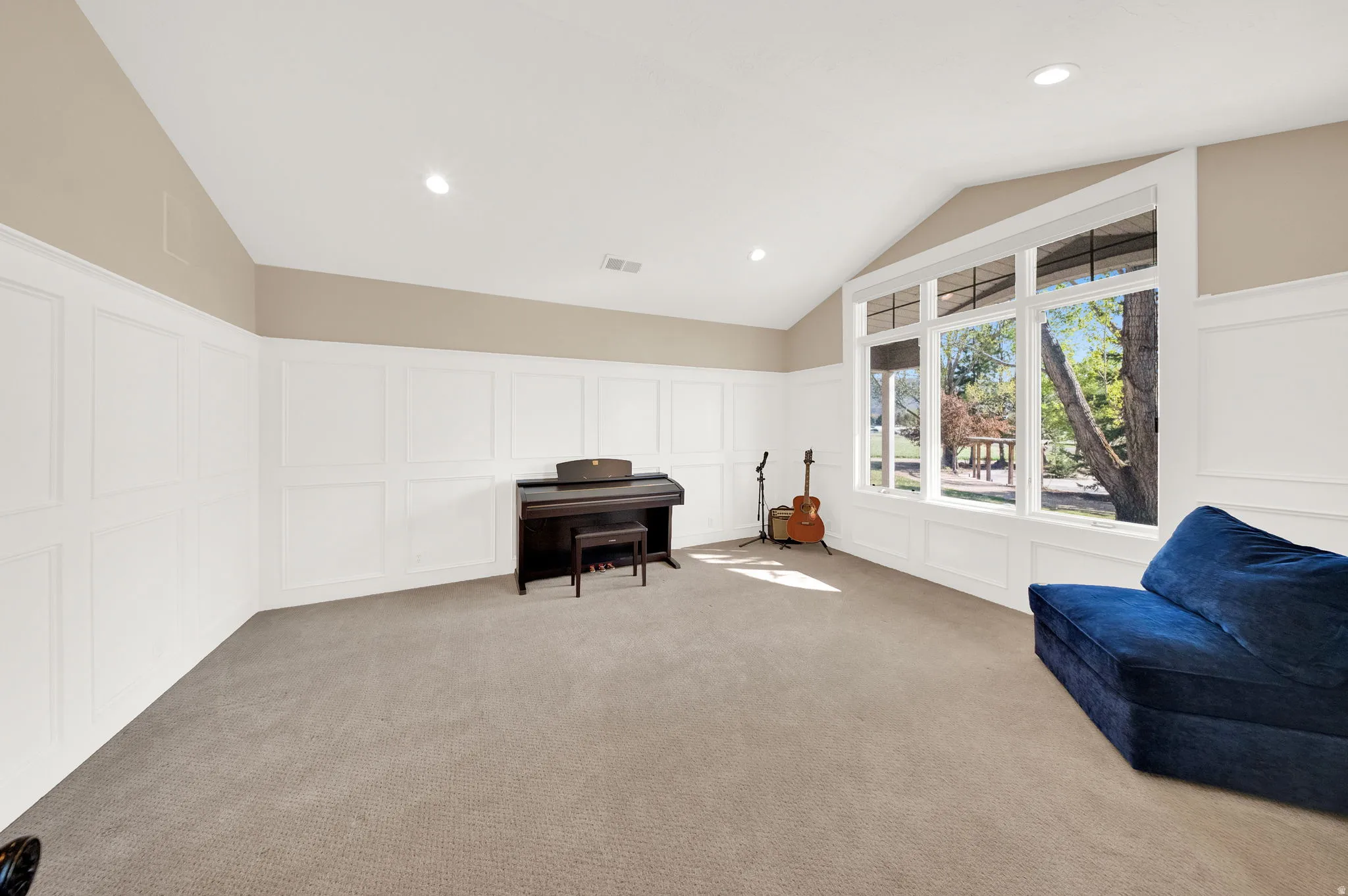 Spacious room featuring vaulted ceilings, recessed lighting, expansive window wall, light-colored carpeting, and wainscoting
