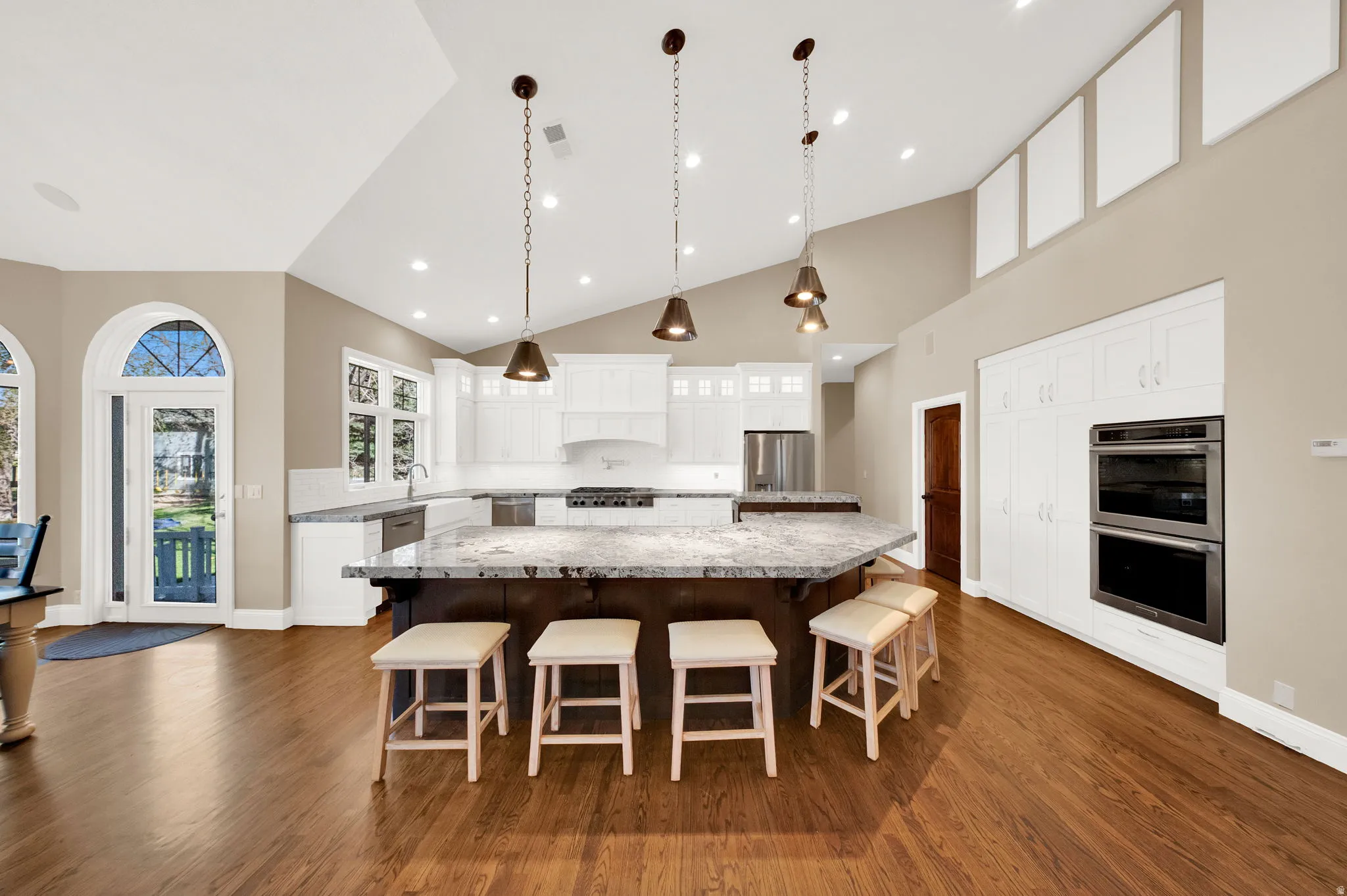 Spacious kitchen featuring an expansive island with seating, white shaker cabinetry, stainless steel appliances, and wood-finish flooring