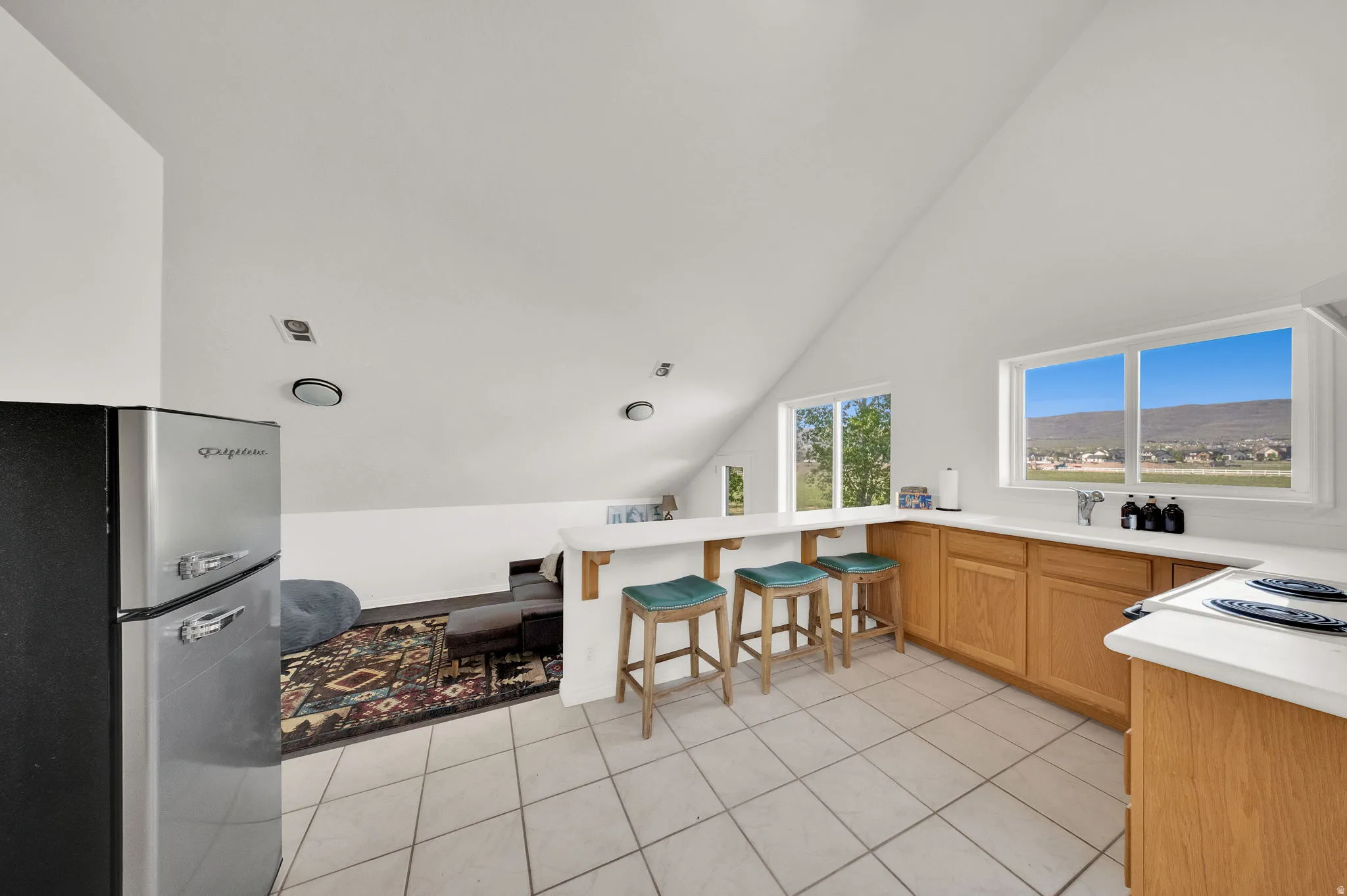 Kitchenette featuring a white tiled floor, wood-finish cabinetry, a white countertop with an integrated sink, a built-in electric cooktop, and a retro-style refrigerator