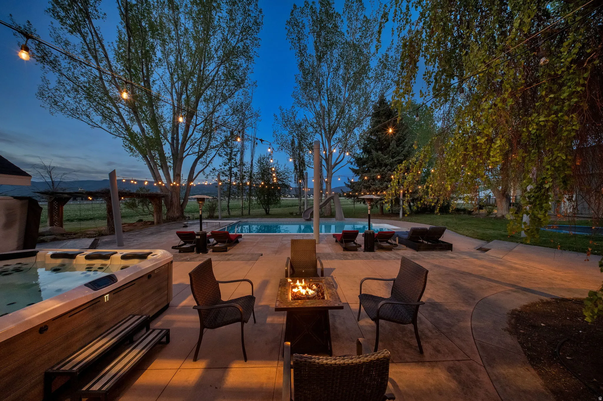 Expansive concrete patio featuring a built-in hot tub, in-ground swimming pool, and a fire pit