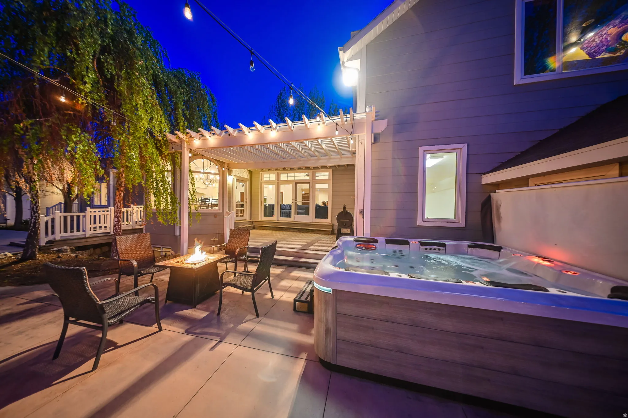 Spacious concrete patio featuring a built-in hot tub, fire pit, and string lighting