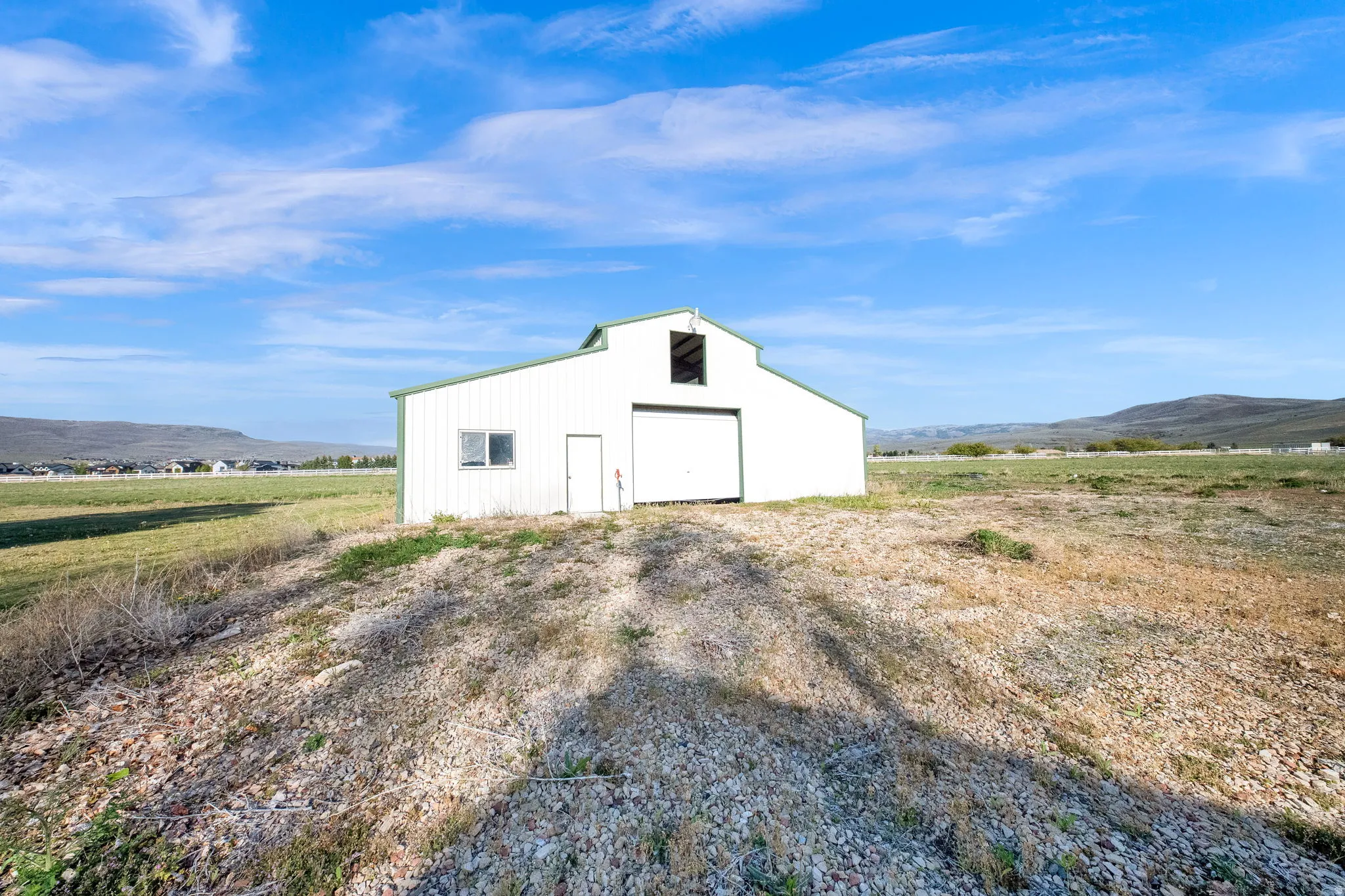 White metal barn with green trim, featuring a large roll-up door, an entry door, and a window