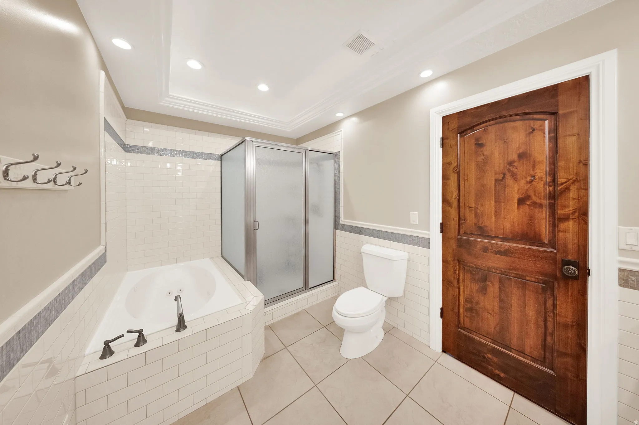 Bathroom featuring an alcove bathtub with subway tile surround, a separate shower enclosure with frosted glass, a standard toilet, and a solid wood door