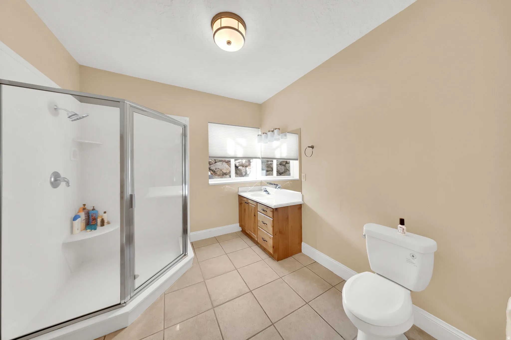 Tiled bathroom featuring a glass-enclosed corner shower, single vanity with wood-finish cabinetry, and a white toilet
